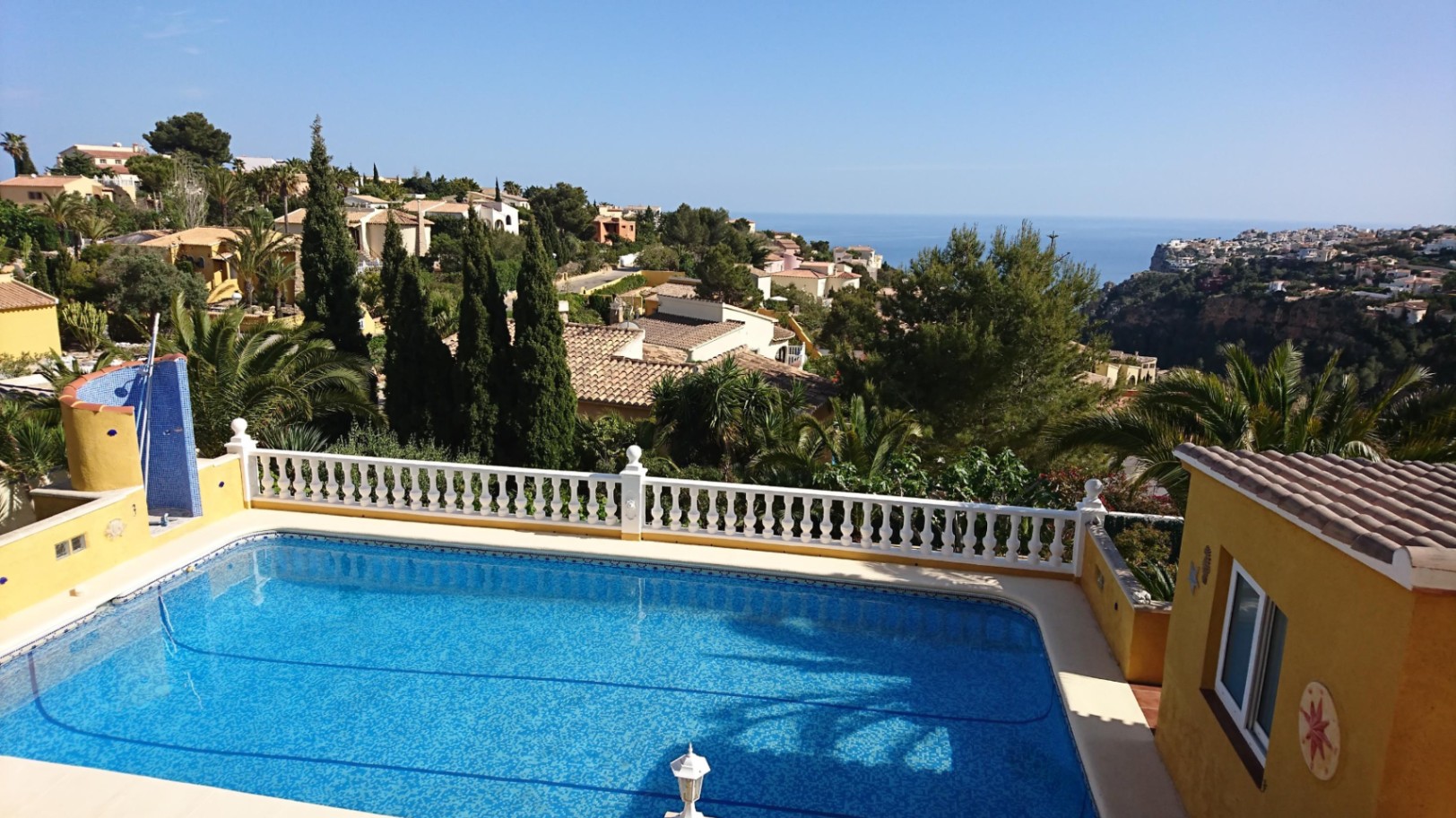 Rectangular swimming pool featuring a white balustrade and outdoor shower, overlooking the Mediterranean Sea and lush coastal landscape.