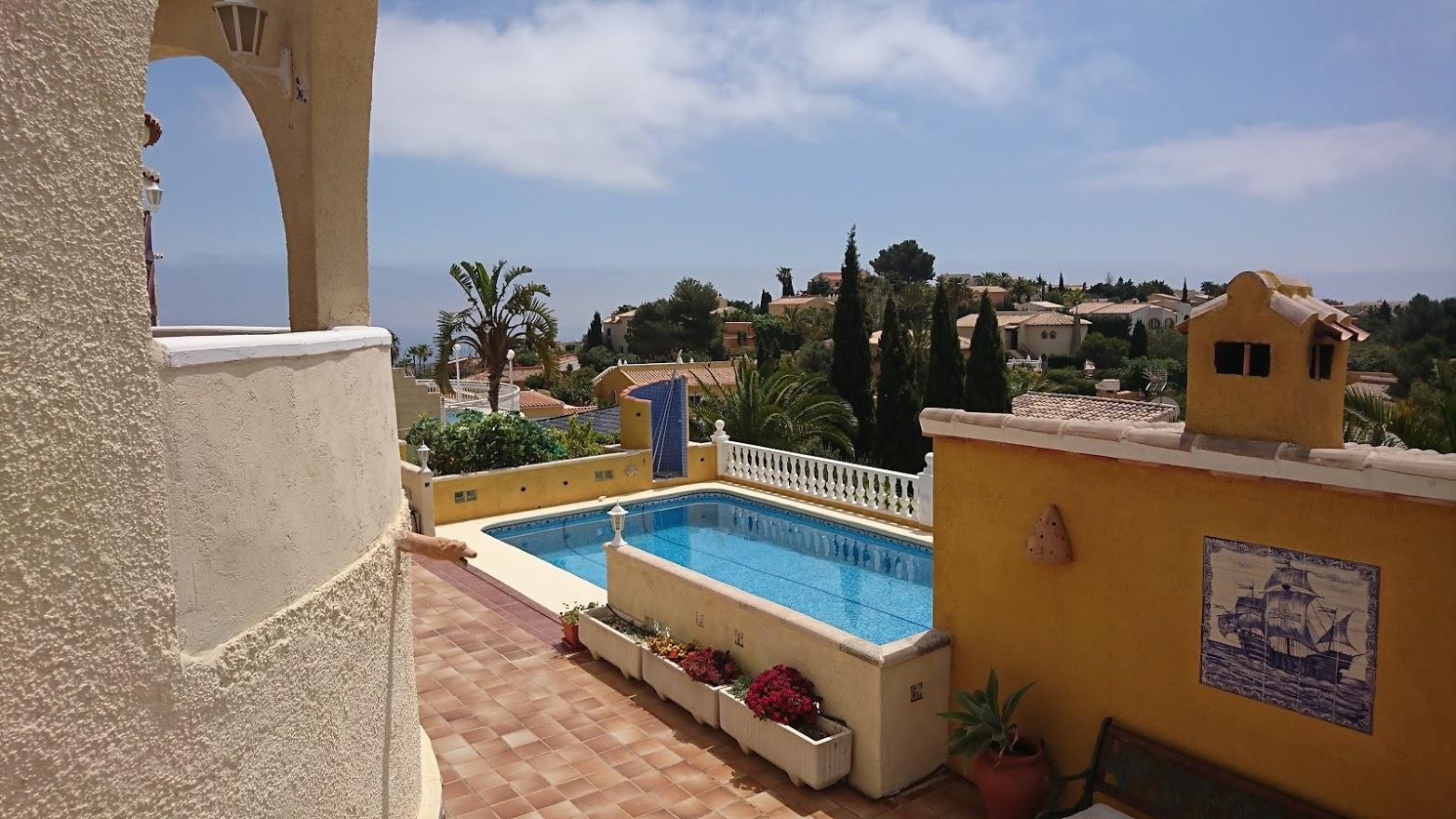 Terrace with terracotta tiling overlooking a rectangular swimming pool, featuring ochre walls with traditional ceramic accents and distant sea views.