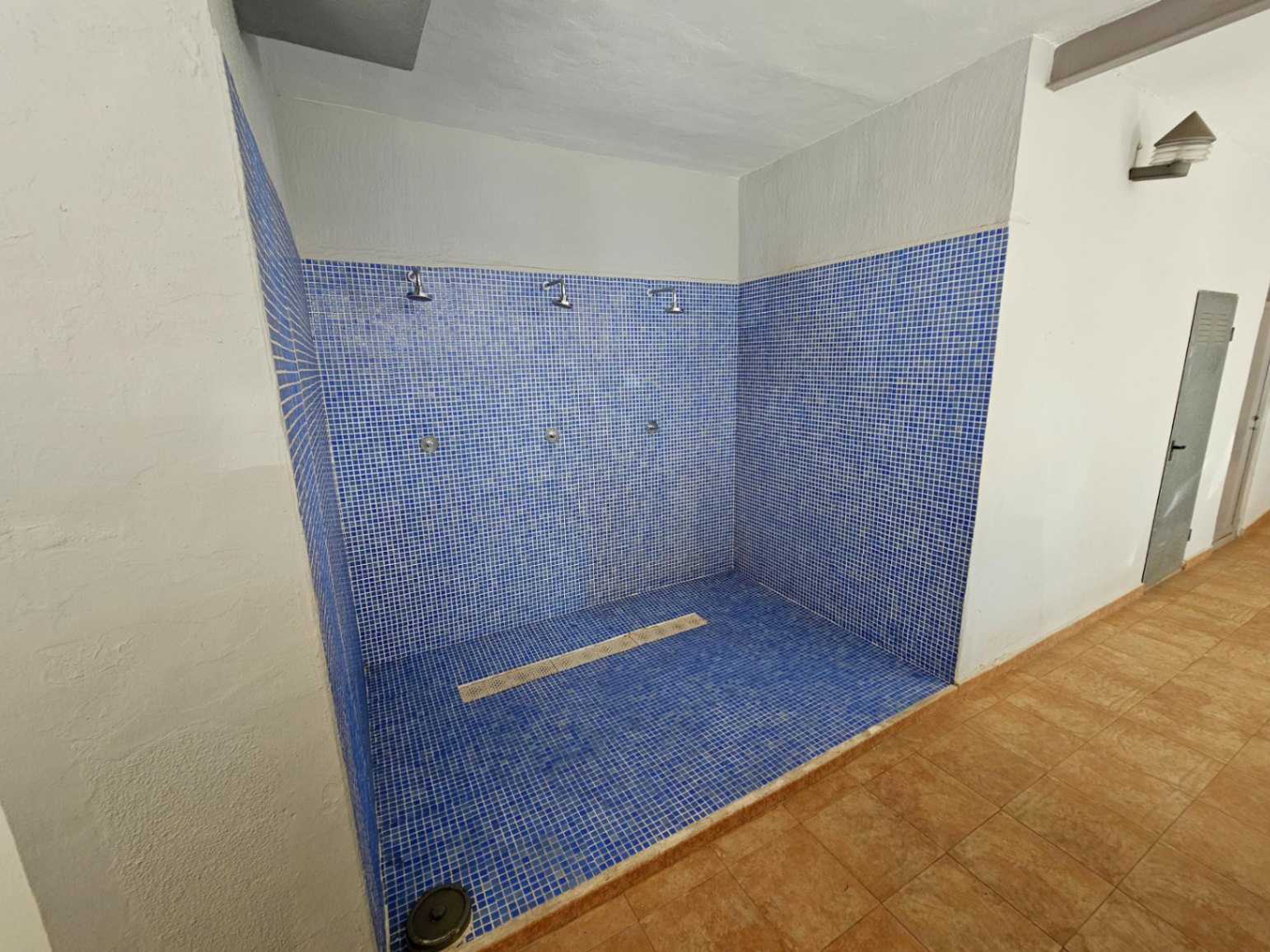 Communal shower area featuring blue mosaic tiling and three shower heads, perfect for rinsing off after the beach. Functional space located within the common facilities.