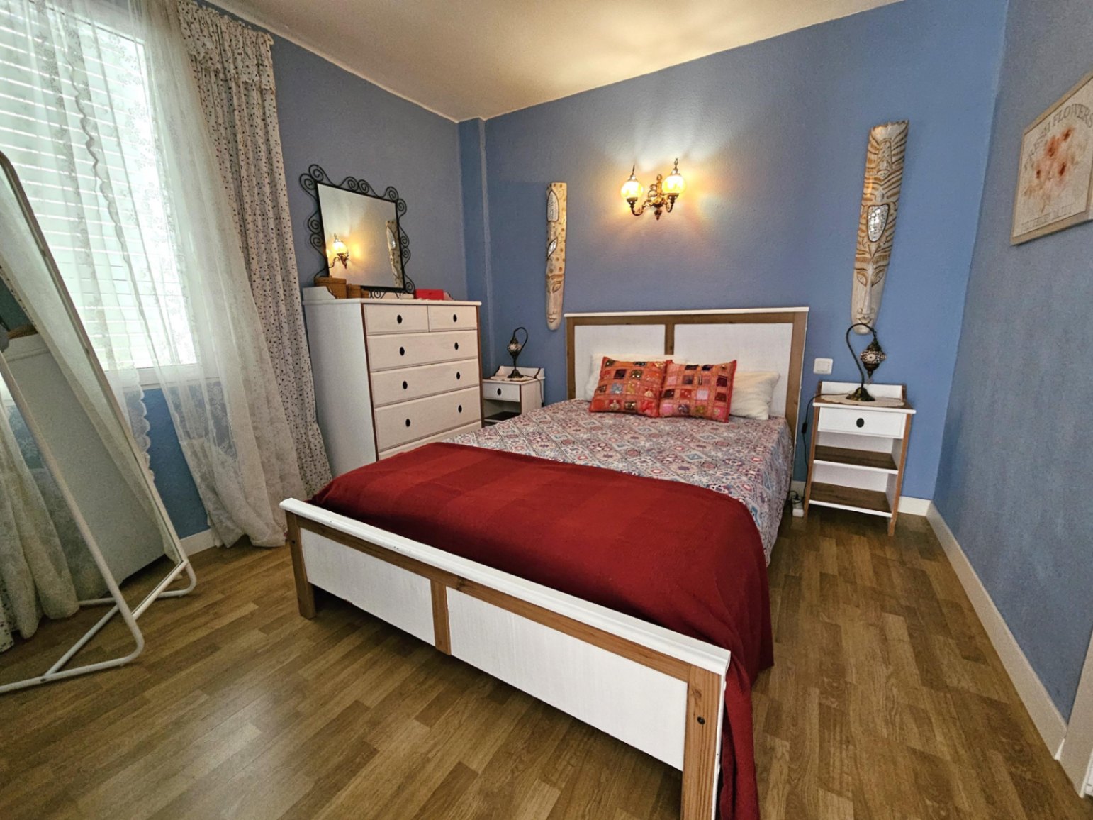 Contemporary bedroom with blue walls, parquet flooring, and white furniture. Features a double bed, chest of drawers, and ample natural light.