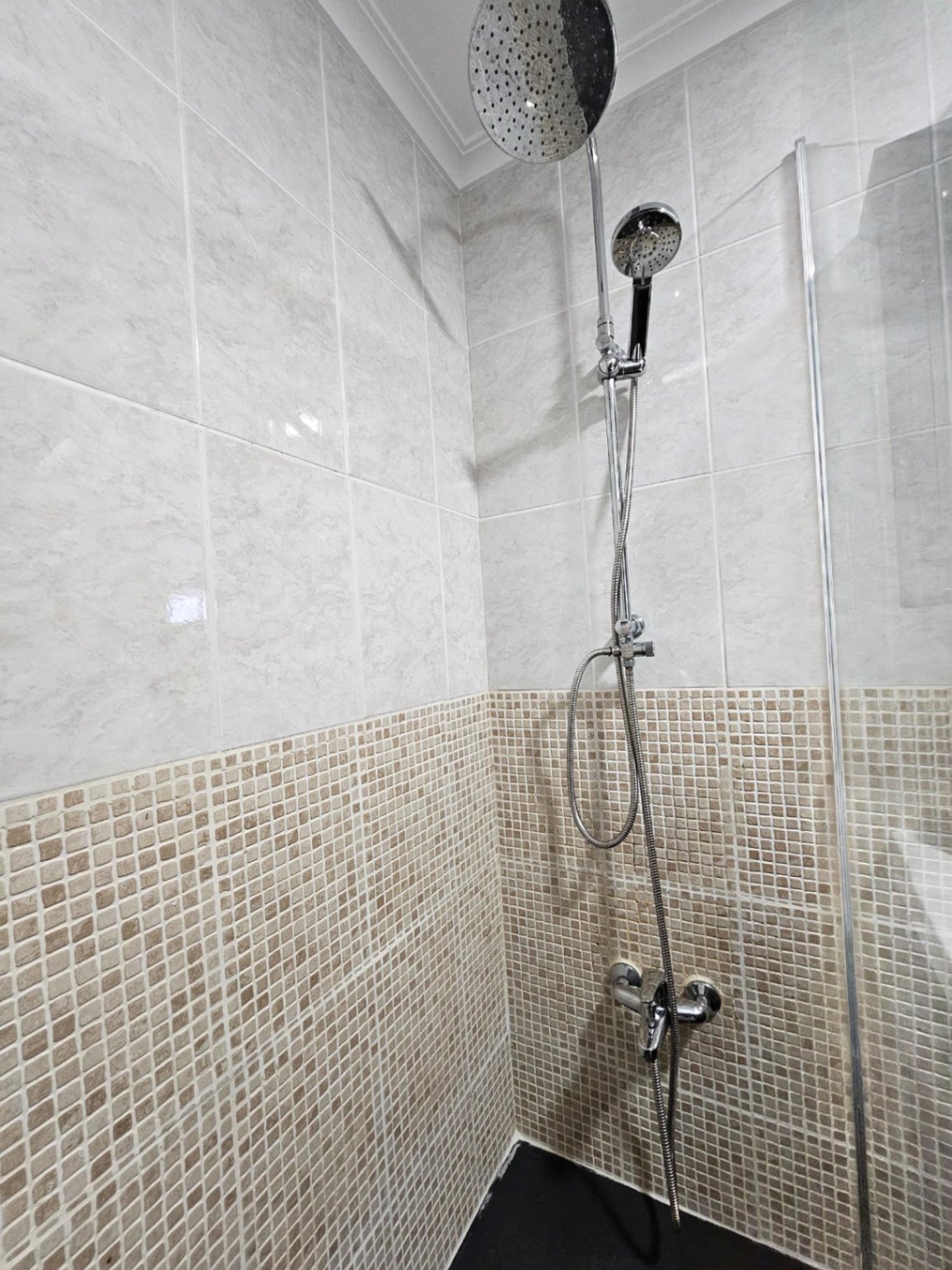 Contemporary shower featuring a dual shower head system, marble-effect wall tiles, and earth-toned mosaic detailing.