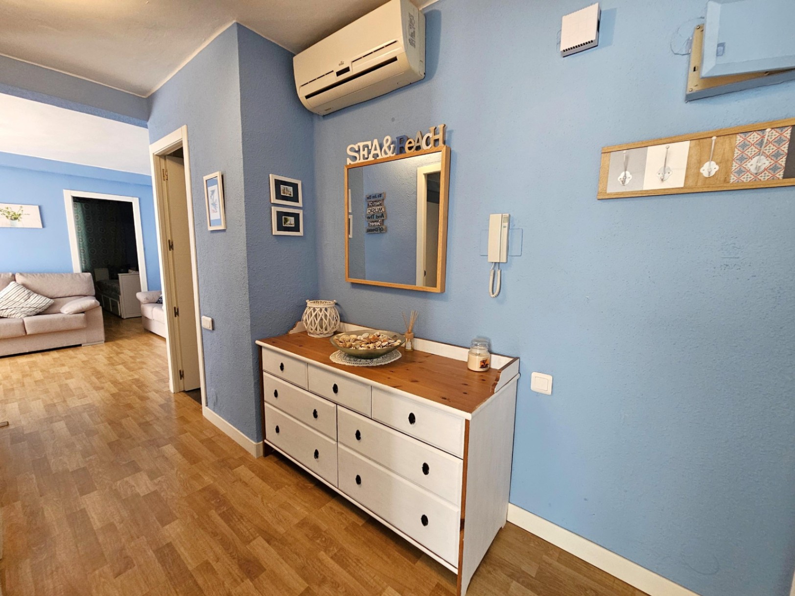Entrance hallway featuring blue walls, parquet flooring, a white wooden dresser, and a wall-mounted air conditioning unit leading to the living area.