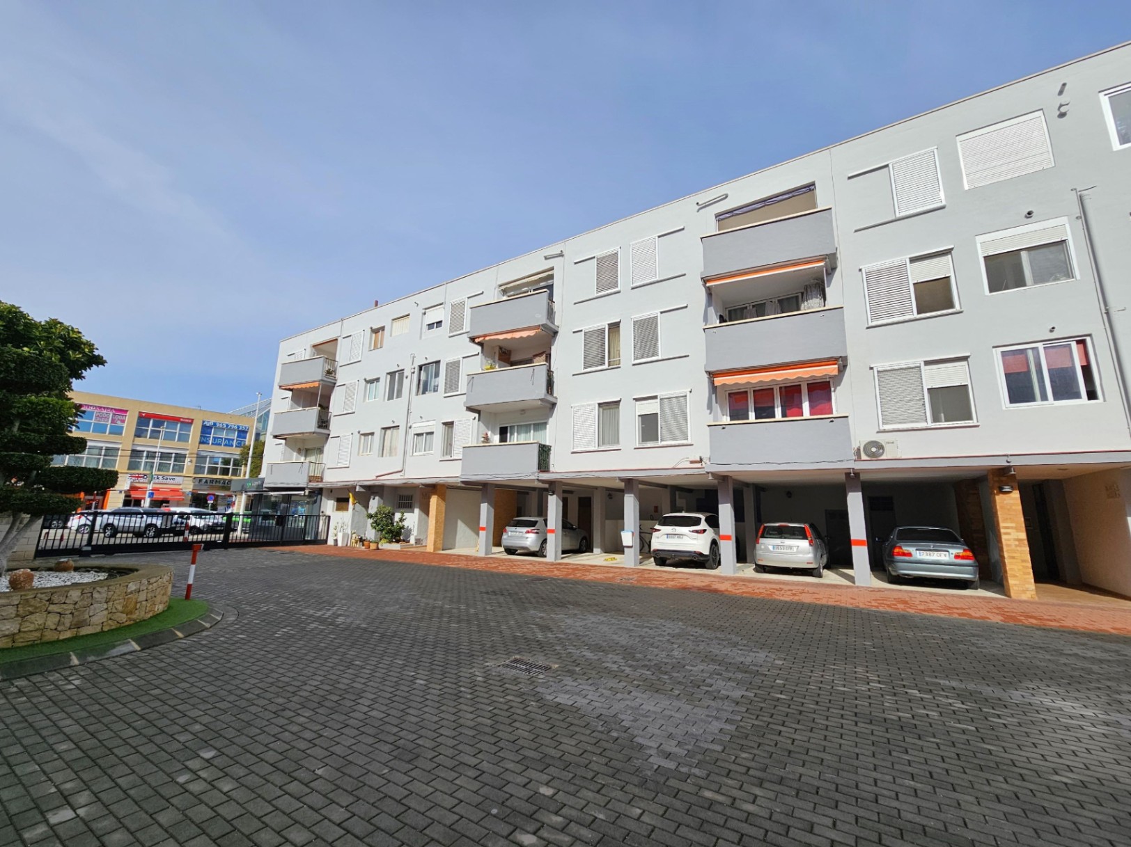 Exterior facade of the apartment building featuring private covered parking spaces on the ground floor and balconies with retractable awnings.