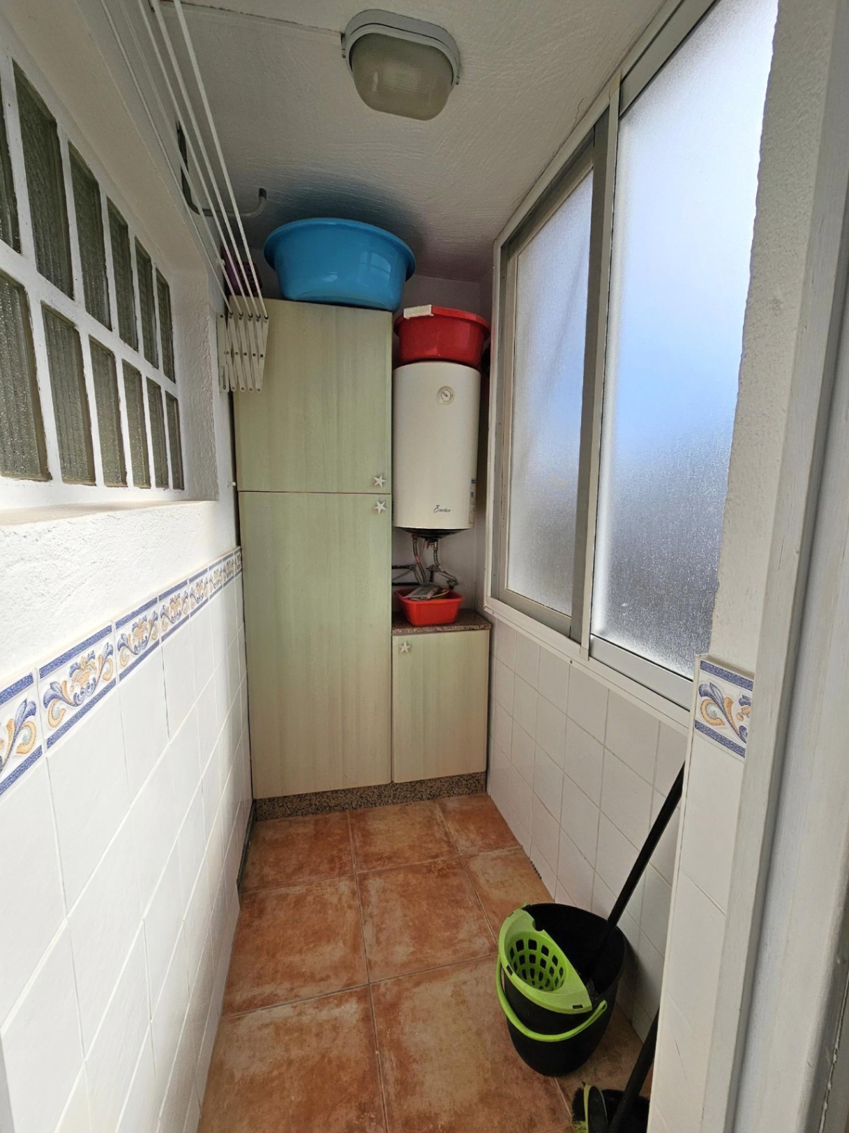 Functional utility room featuring storage cabinetry, an electric water heater, wall-mounted drying rack, and rustic tile flooring.