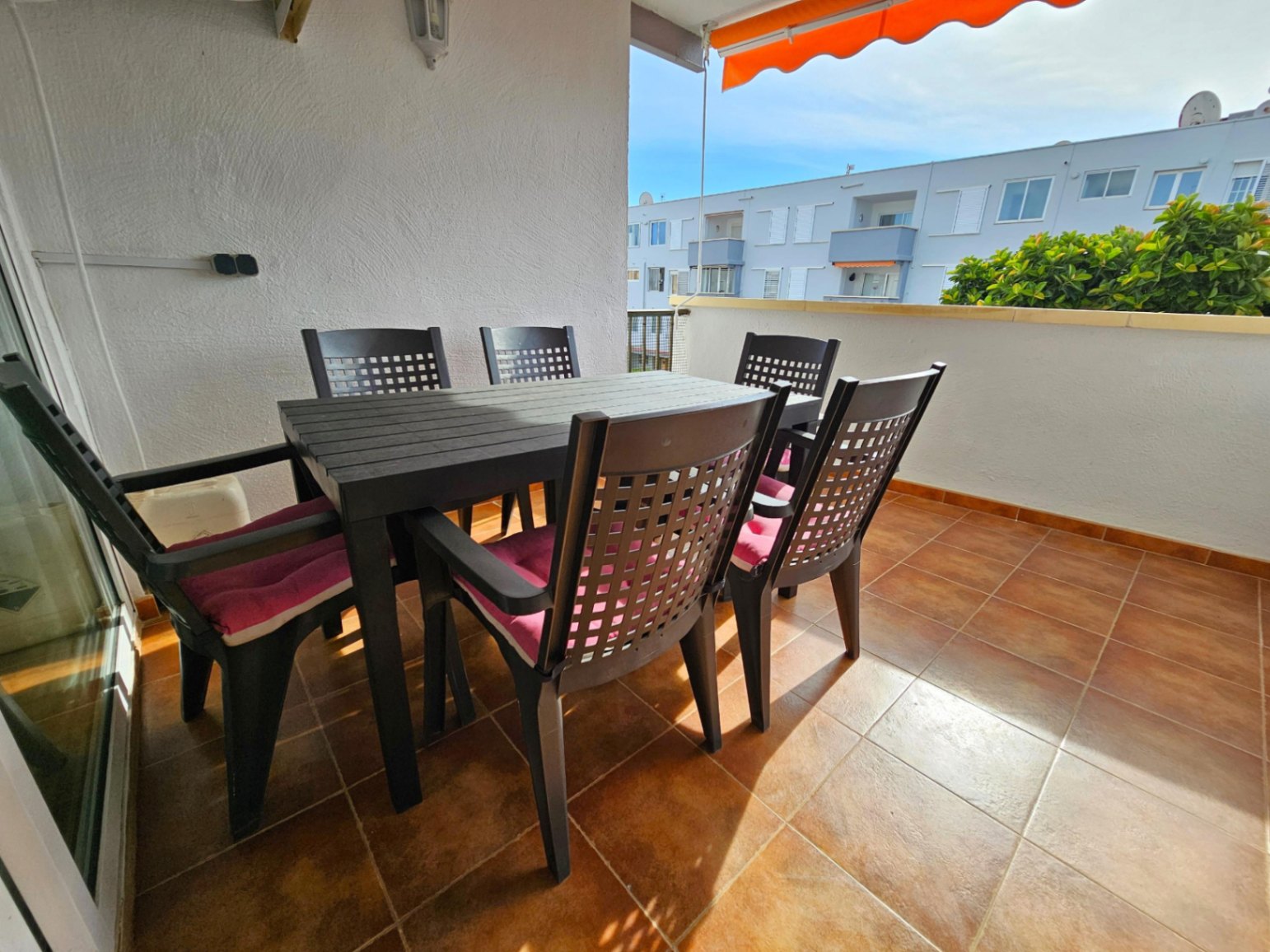 Outdoor terrace featuring terracotta-style floor tiles, a six-seater dining set with cushions, and a retractable orange awning for shade.