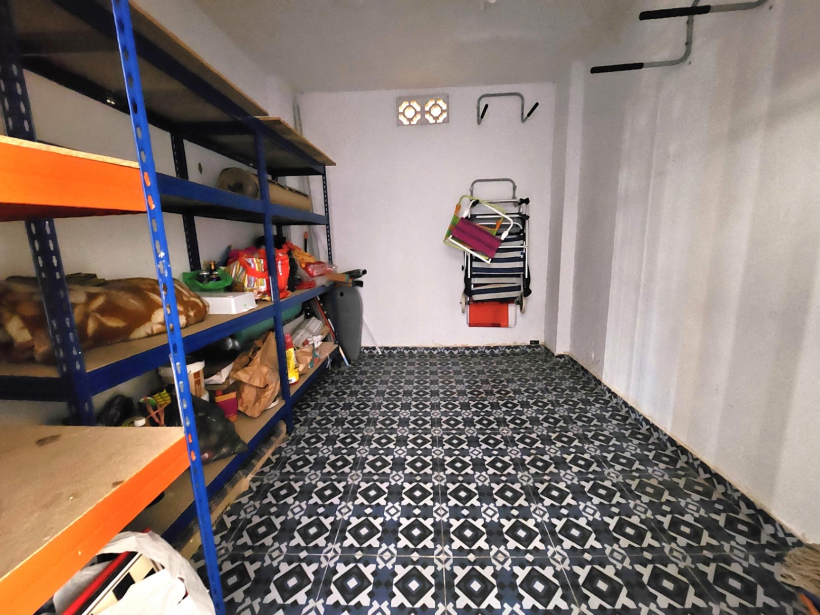 Private 12 m² storage unit featuring heavy-duty metal shelving, geometric patterned floor tiles, and wall-mounted storage hooks.
