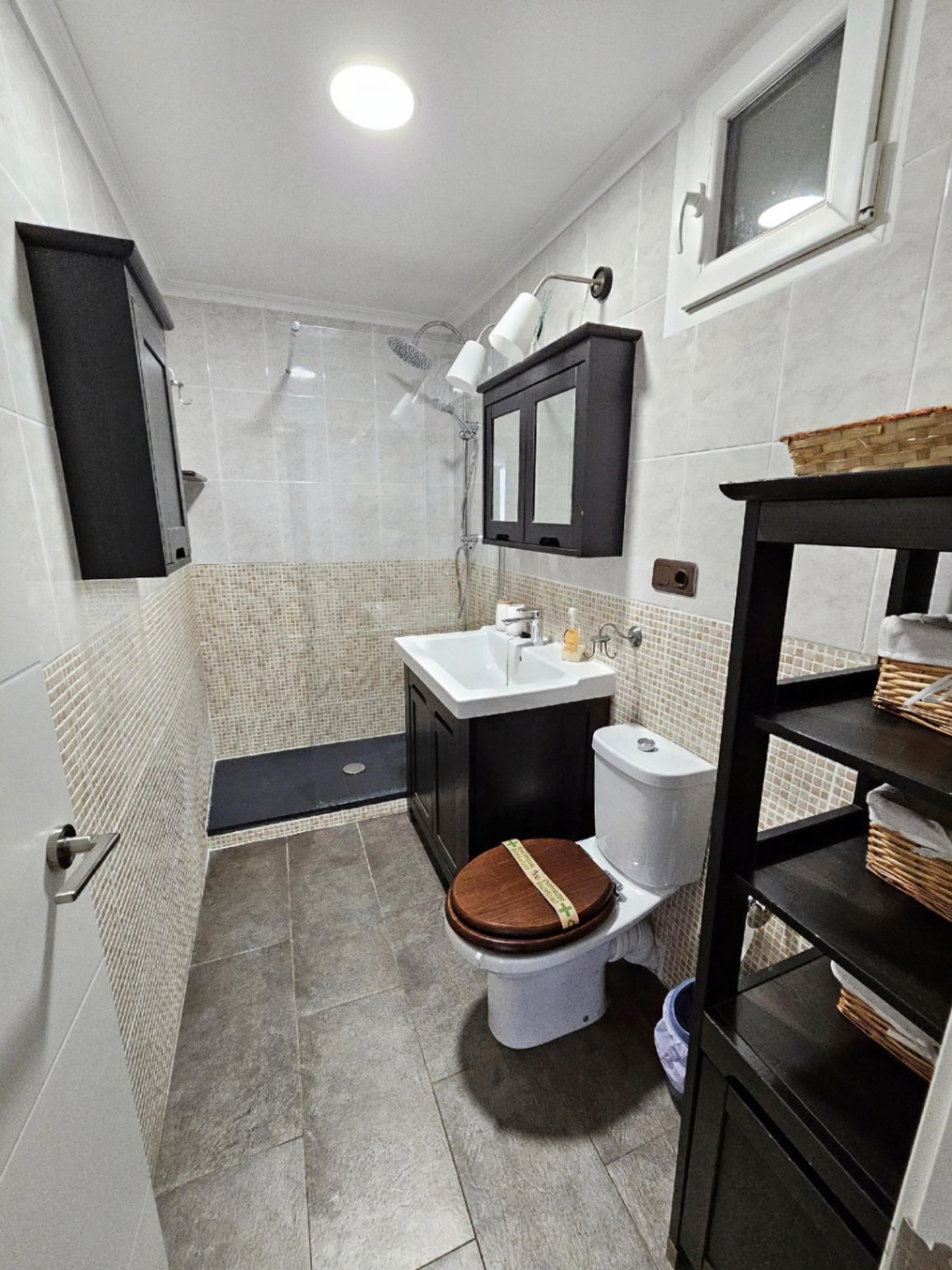 Renovated bathroom featuring a walk-in shower with mosaic tiling, dark wood cabinetry, and a contemporary white ceramic vanity.
