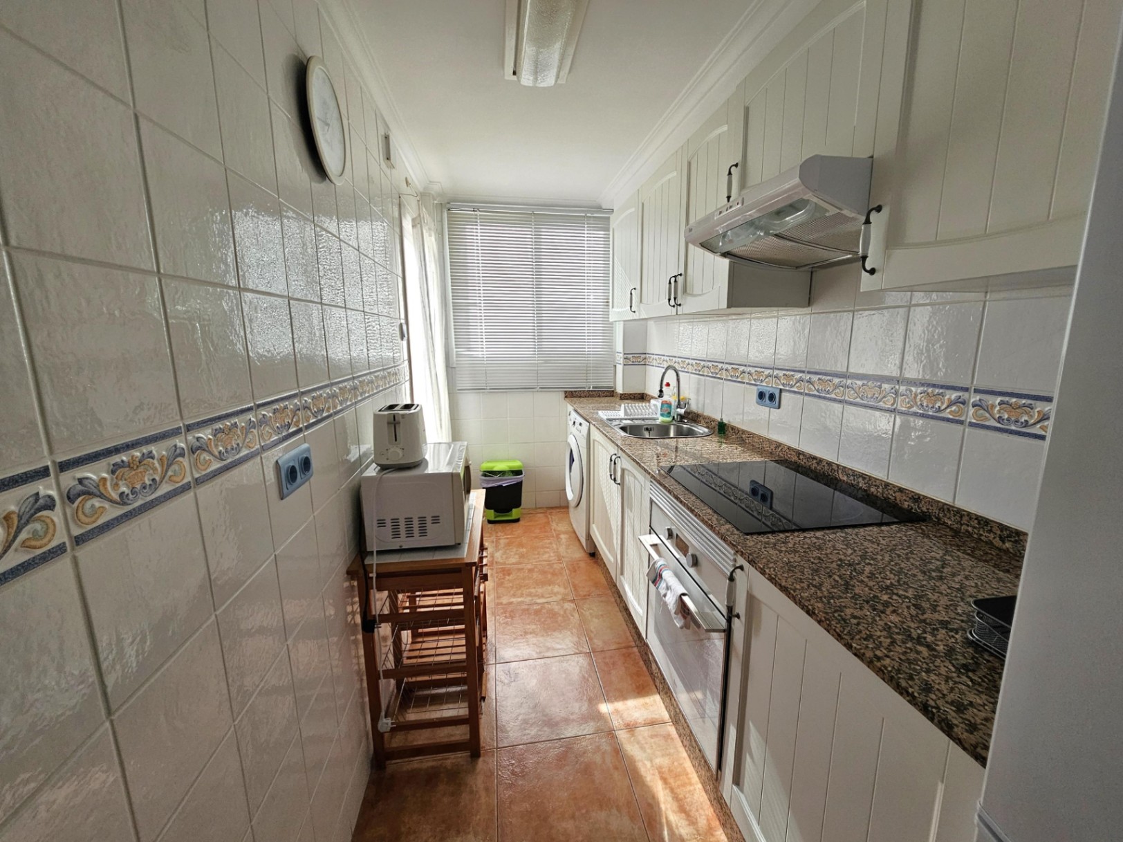 Renovated galley kitchen featuring granite countertops, white cabinetry, and integrated appliances. A large window provides ample natural light.