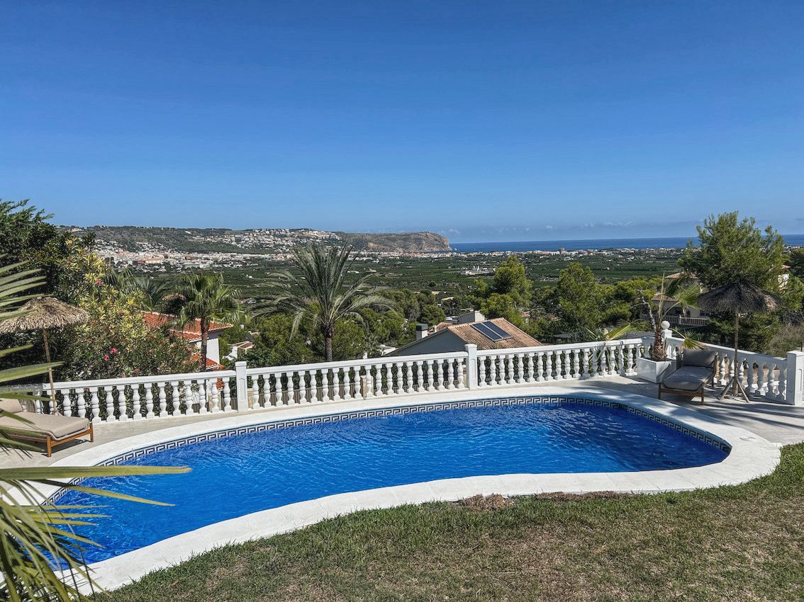 Curved outdoor swimming pool with white balustrades, featuring panoramic views of the valley and the Mediterranean coastline.