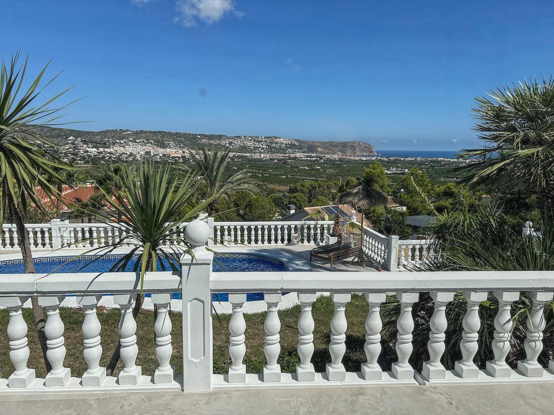 Elevated terrace featuring a white balustrade with panoramic views of the valley and Mediterranean Sea, overlooking the private pool and lush palm trees.