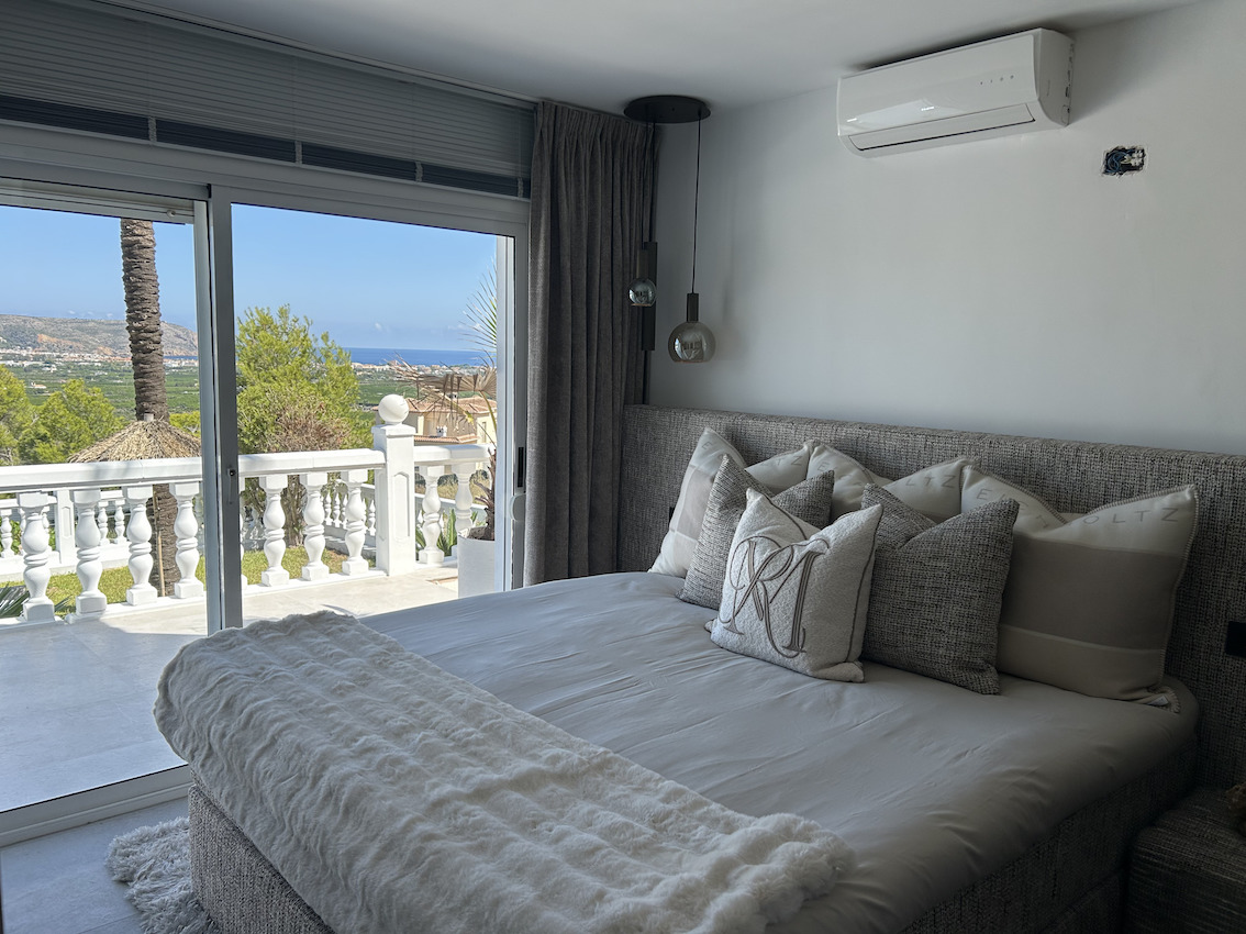 Master bedroom featuring an upholstered headboard, split air conditioning, and sliding doors opening to a private terrace with sea and valley views.