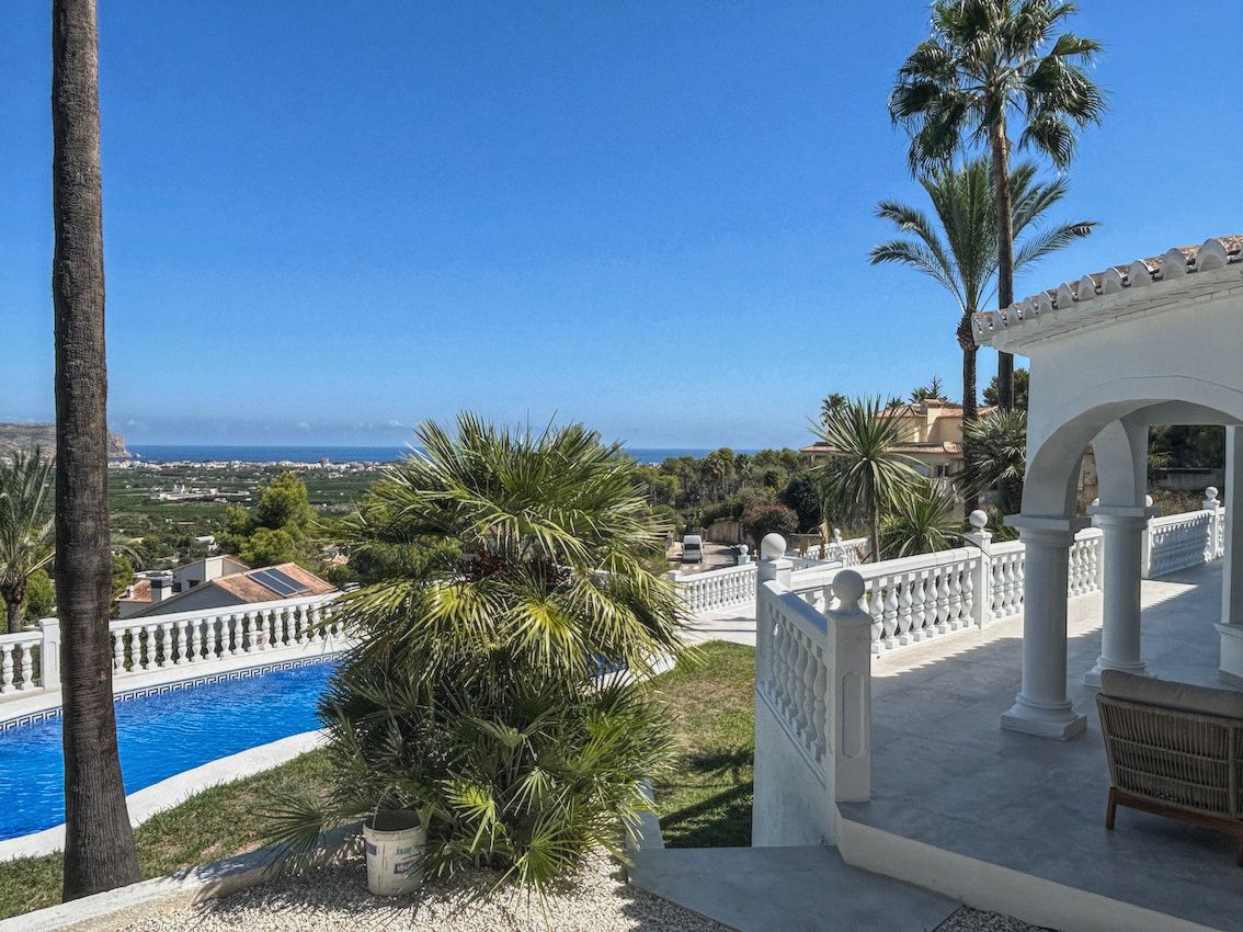 Terrace with white balustrades and an arched porch offering panoramic sea and valley views, surrounded by palms and the swimming pool area.