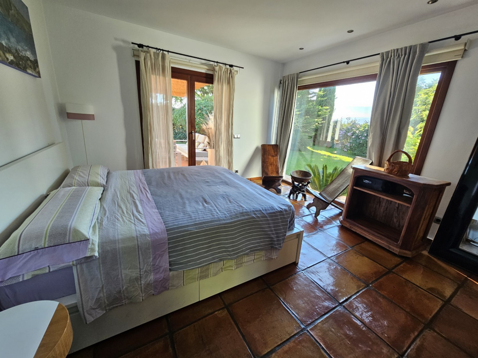 Bright bedroom featuring handmade clay tile flooring, large windows with garden views, and direct access to the outdoor terrace.