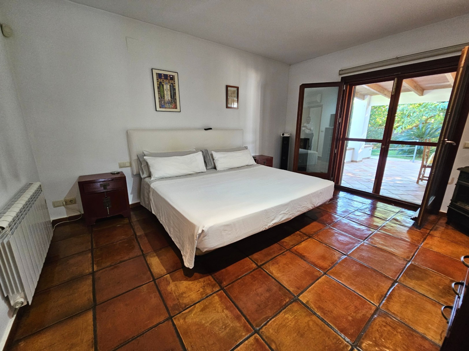Bright bedroom featuring handmade terracotta tile flooring, a large bed, and direct access to the outdoor terrace through floor-to-ceiling glass doors.