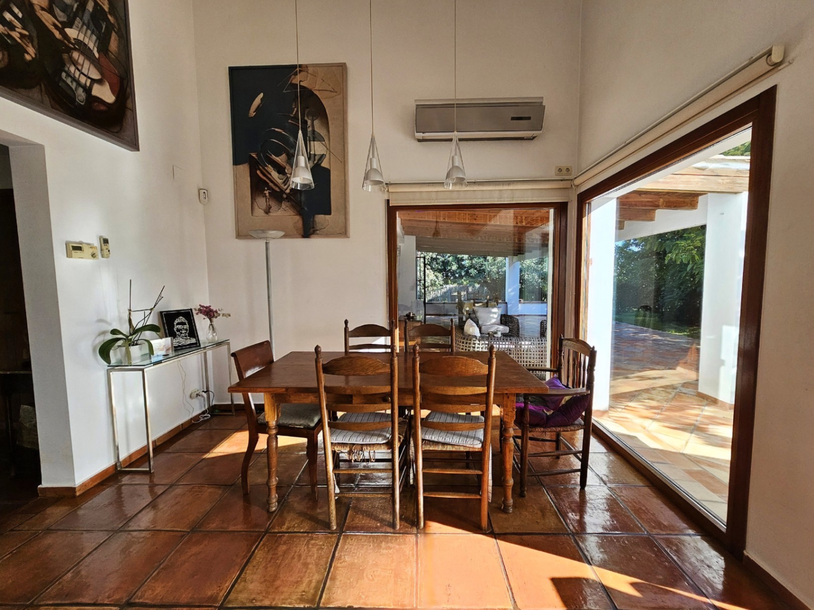Bright dining area featuring handmade terracotta floors, a solid wood table set, and large glass doors offering direct views and access to the terrace.