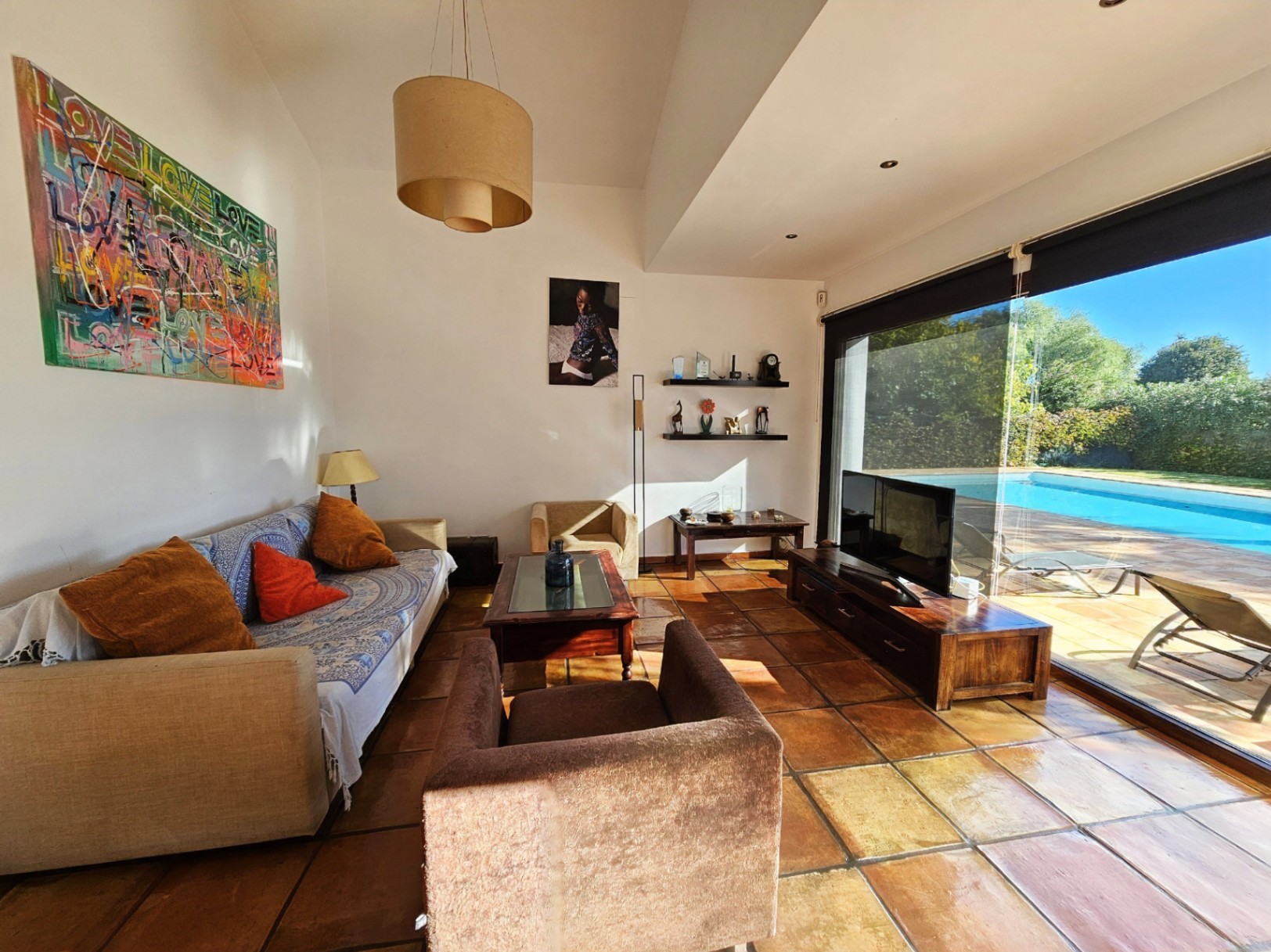 Bright living room featuring handmade clay tile flooring and large security glass doors with direct views of the pool and garden.