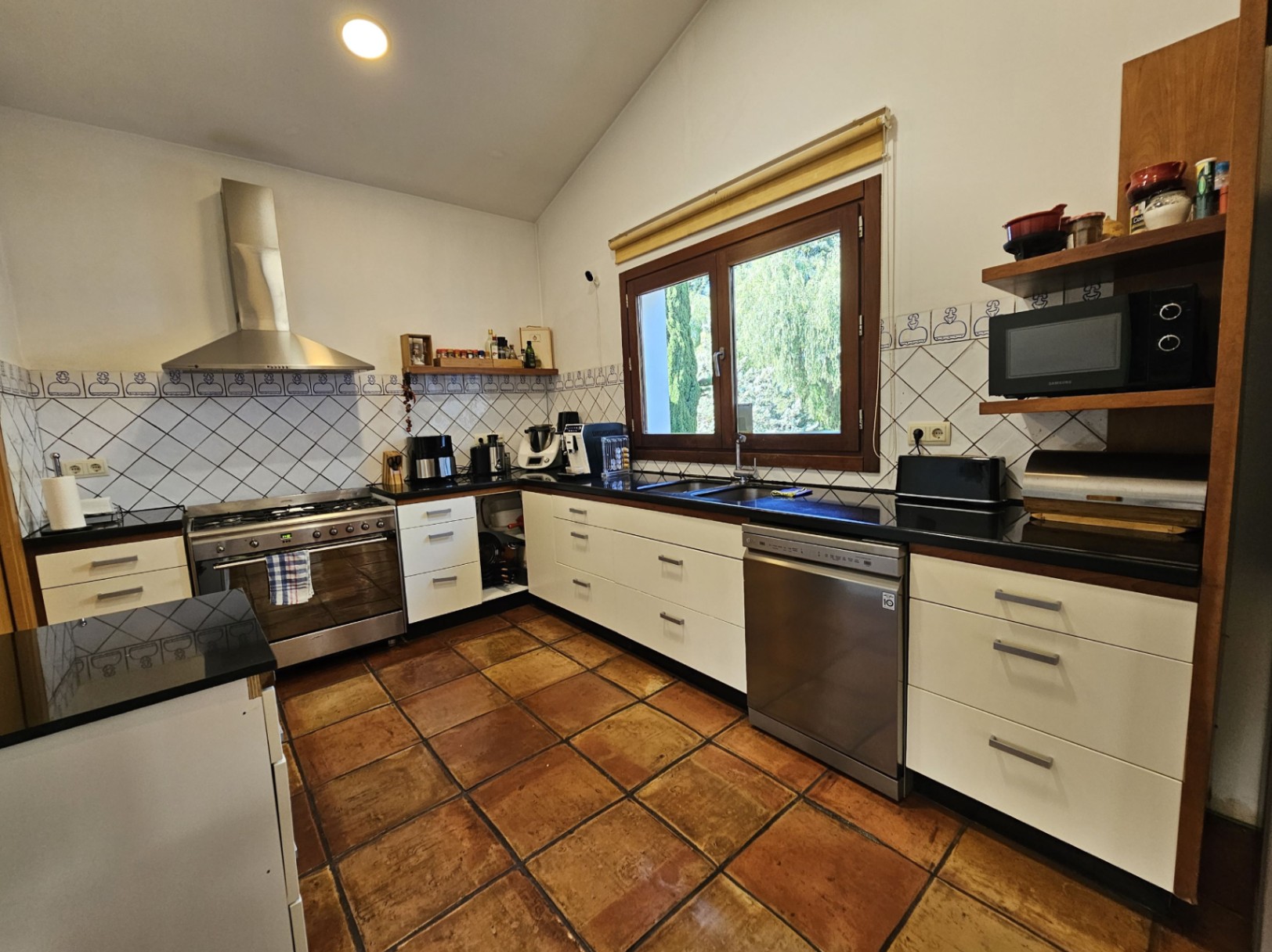 Fully equipped kitchen featuring handmade terracotta floor tiles, dark countertops, and stainless steel appliances, including a large range cooker and integrated dishwasher.