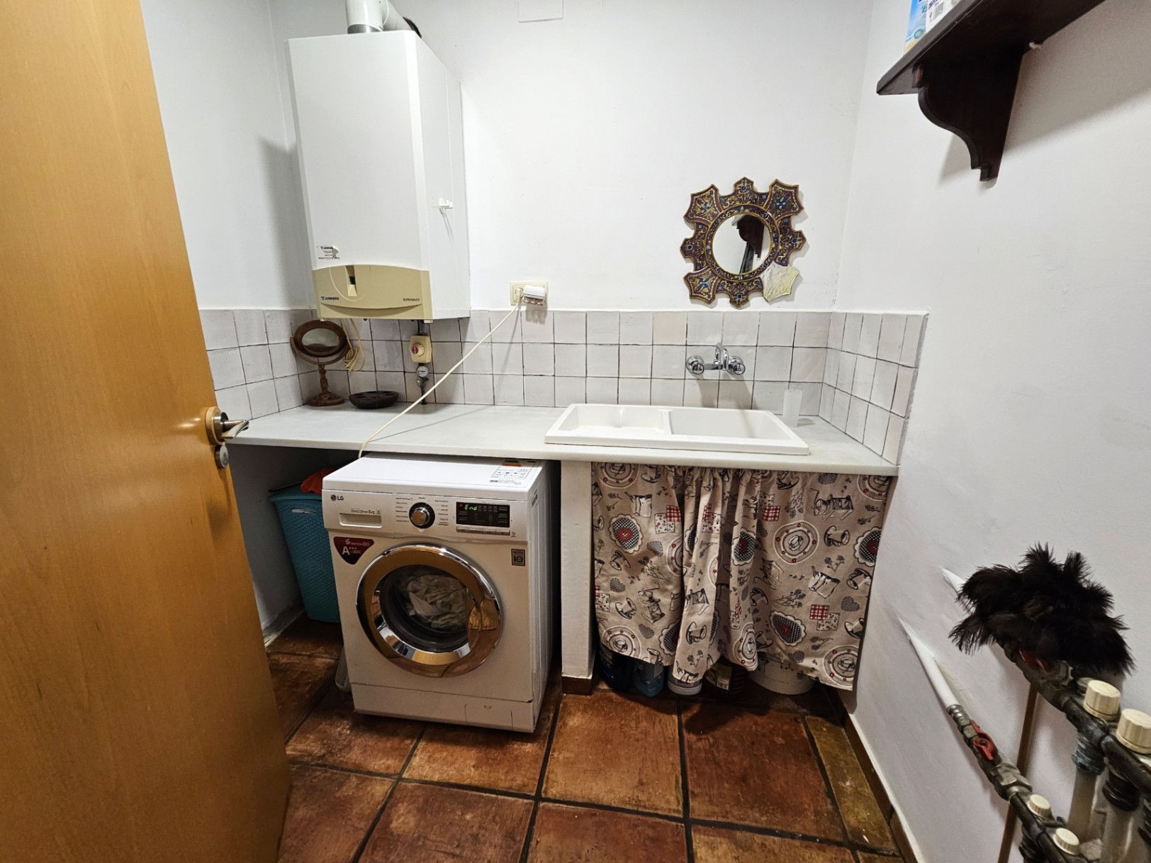 Functional laundry room featuring handmade clay tile flooring, an LG washing machine, a double sink, and a wall-mounted boiler above the white workspace.
