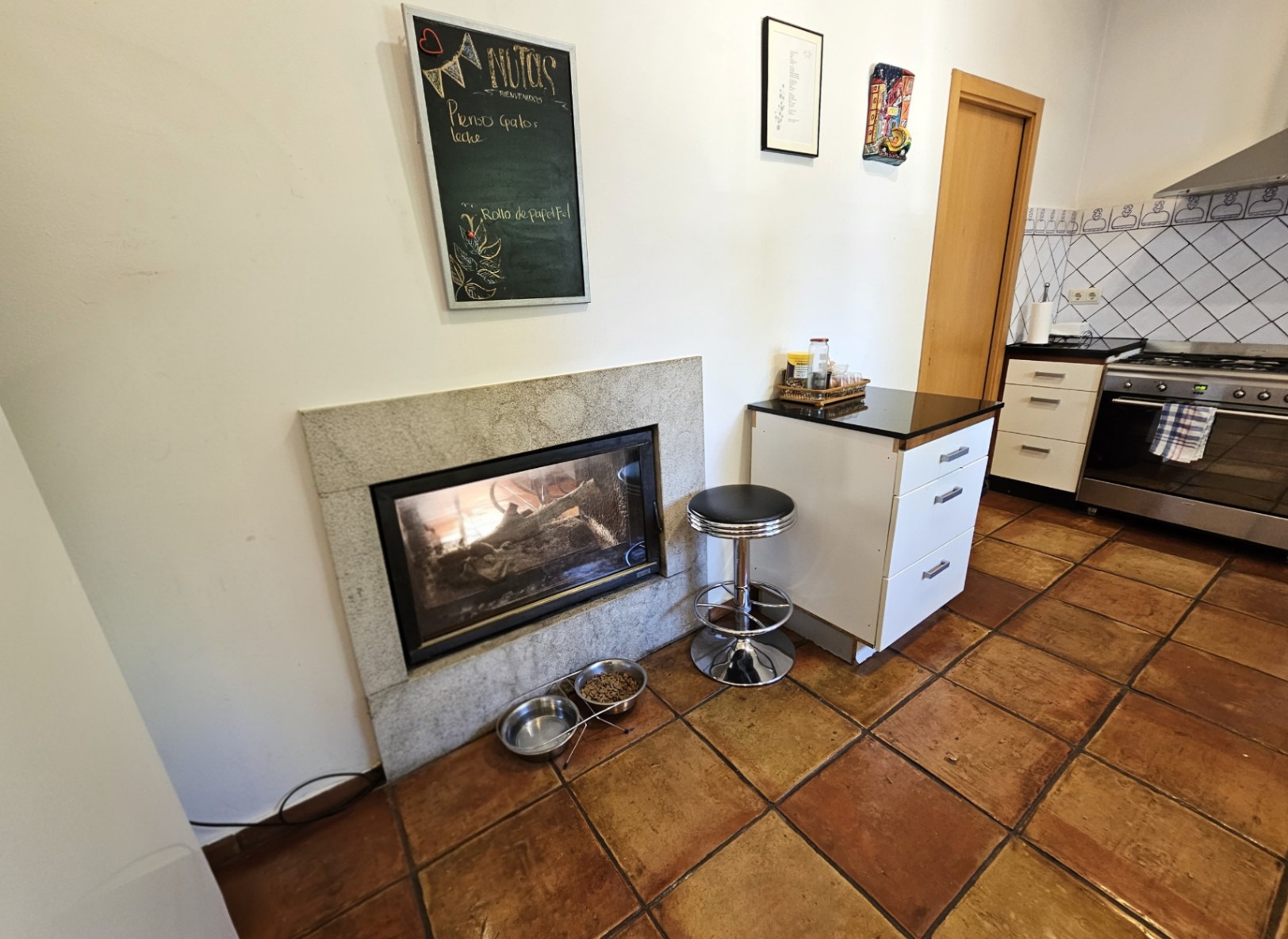 Kitchen area showcasing handmade clay flooring, a built-in fireplace with stone trim, and white cabinetry paired with professional stainless steel appliances.