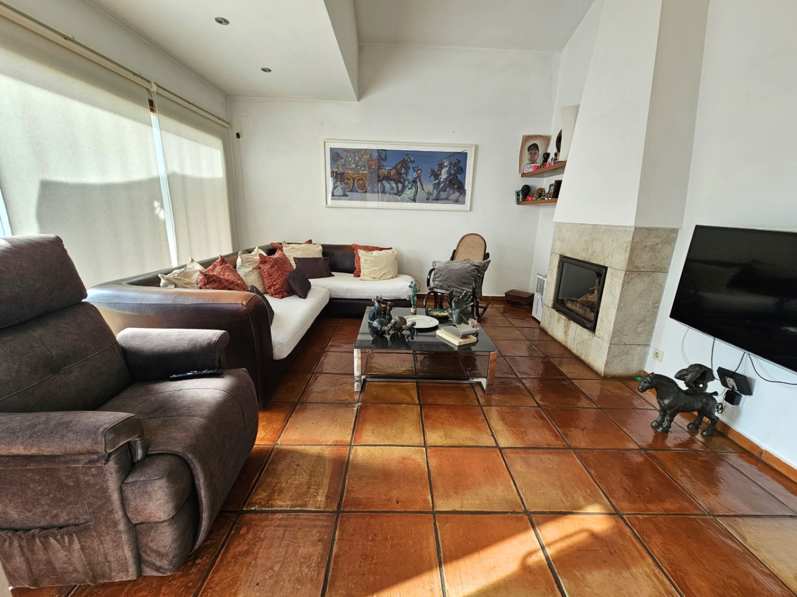 Living area featuring handmade clay tile flooring, a stone-clad built-in fireplace, and large windows providing abundant natural light.