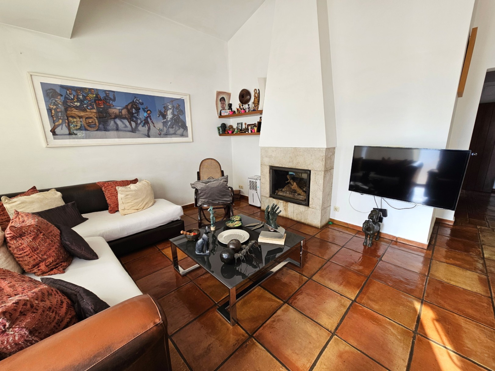 Living area featuring handmade terracotta tile flooring and a built-in stone fireplace. The space includes high ceilings, modern furnishings, and natural light.
