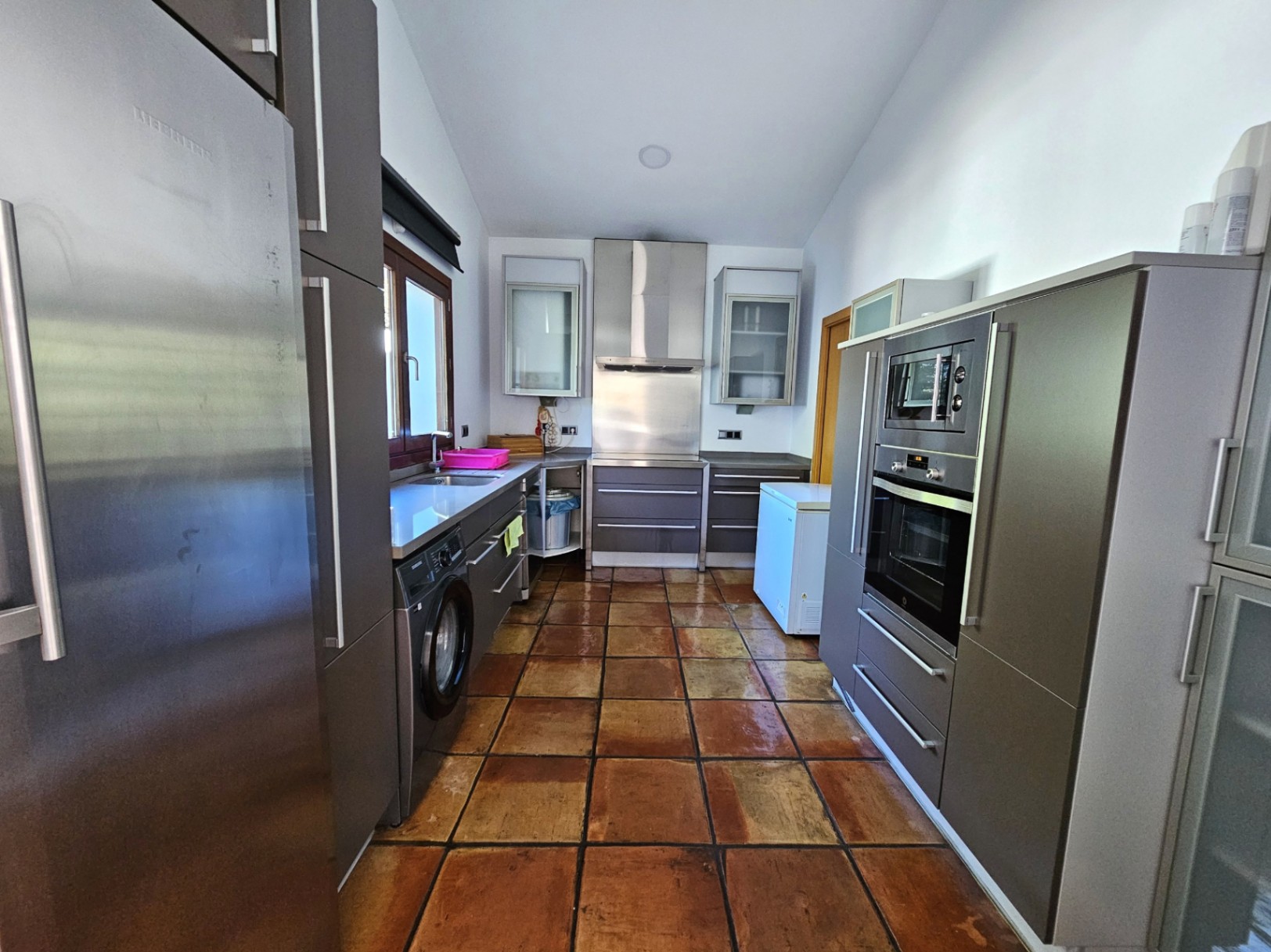 Modern kitchen featuring matte grey cabinetry, integrated stainless steel appliances, and traditional handmade clay tile flooring for a rustic yet refined look.