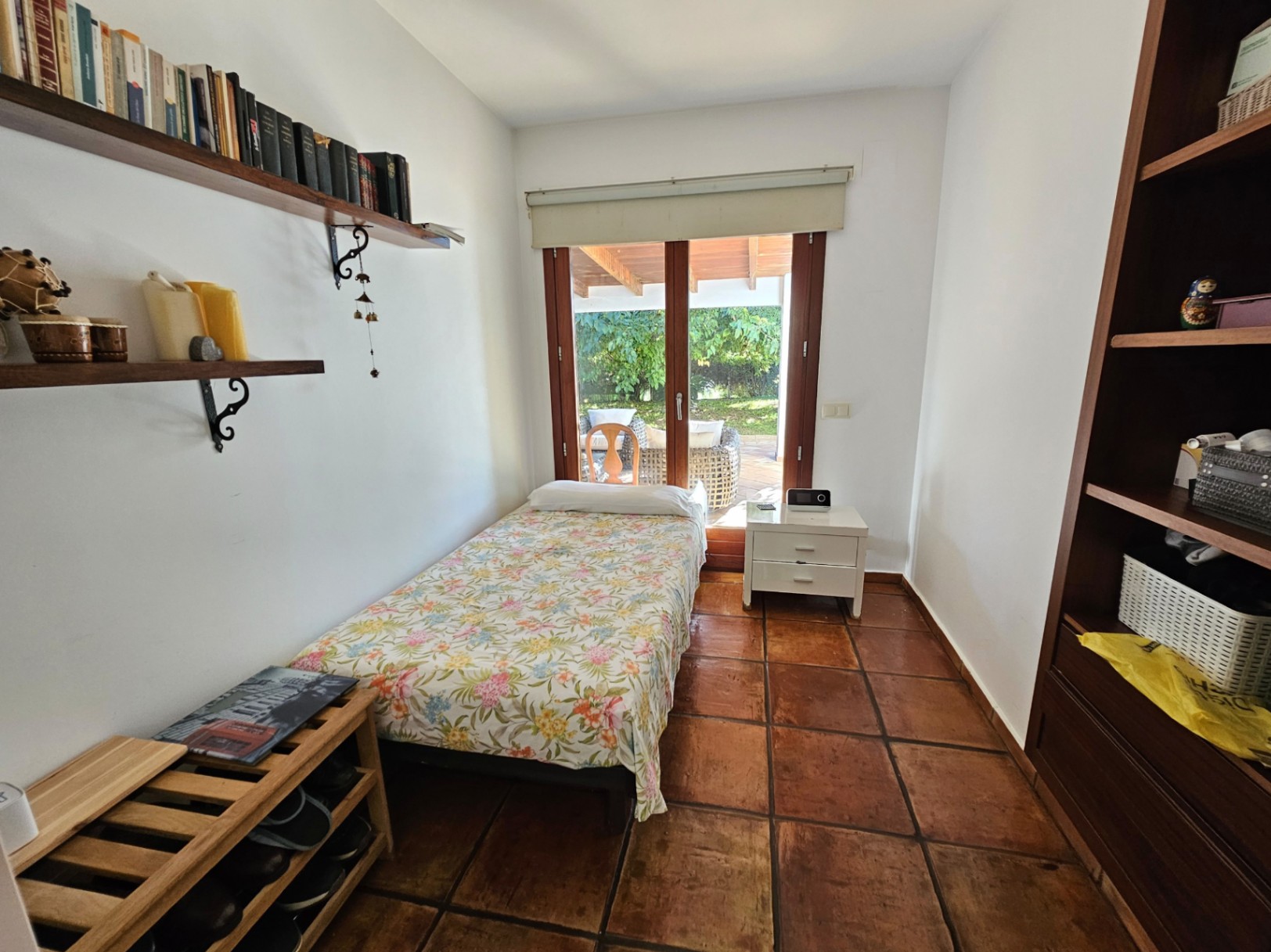 Single bedroom featuring handmade terracotta tile flooring, wooden shelving, and direct access to the covered terrace through large glass doors.