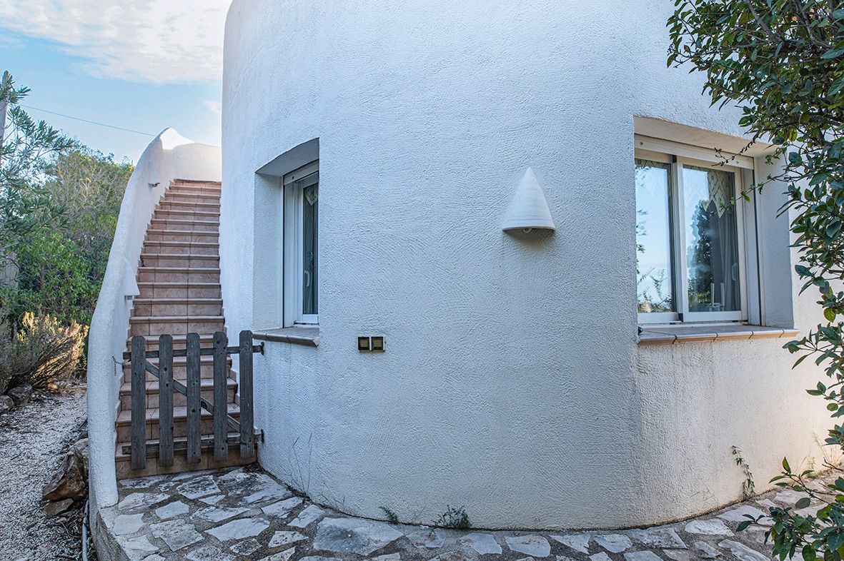 Curved Mediterranean facade featuring white stucco walls, an exterior tiled staircase with a wooden gate, and double-glazed windows.