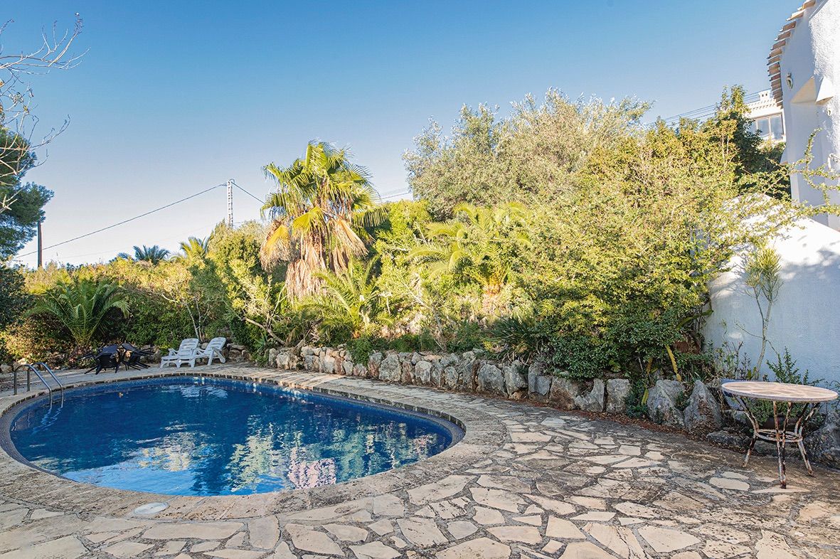 Kidney-shaped swimming pool featuring a natural stone terrace and a lush Mediterranean garden. The area includes sun loungers and a rustic stone retaining wall.