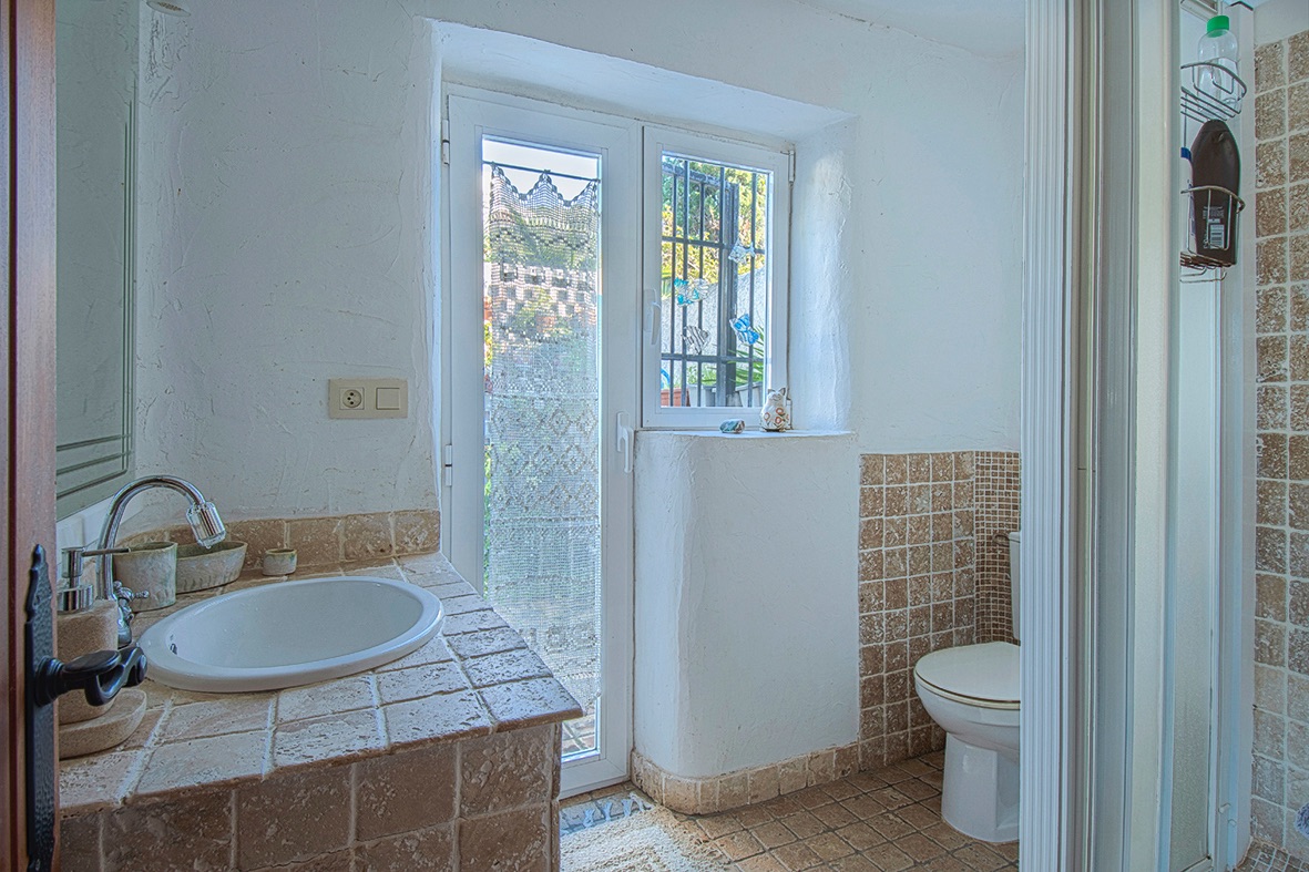 Rustic bathroom featuring a tiled built-in vanity with an oval sink, textured white walls, and a glass door providing natural light and outdoor access.