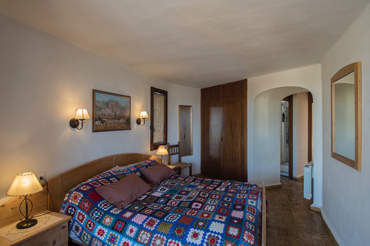 Rustic bedroom featuring built-in wooden wardrobes, terracotta-style flooring, and an arched doorway leading to the ensuite bathroom.