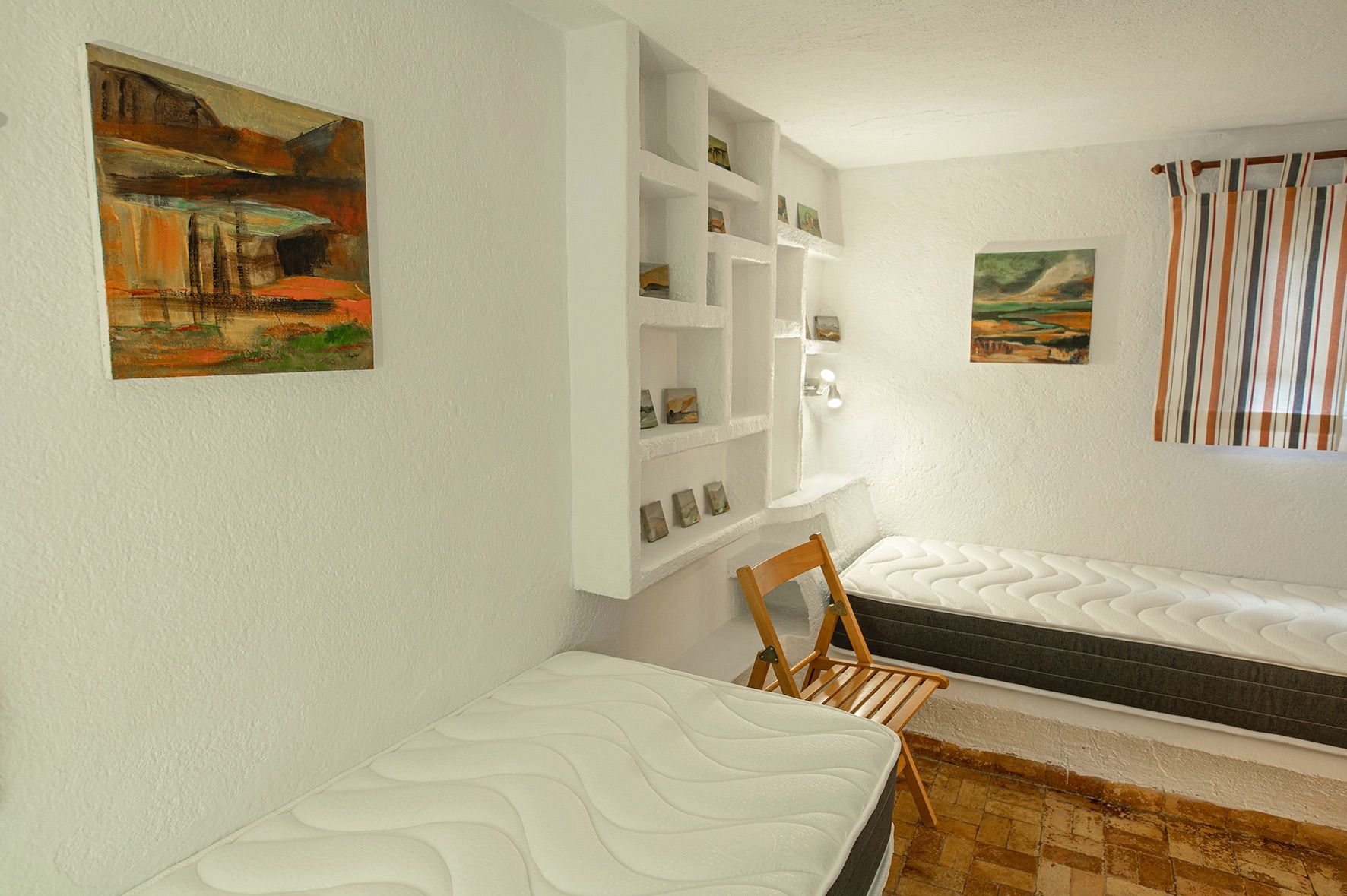 Rustic bedroom featuring twin beds, integrated built-in wall shelving, and traditional terracotta tile flooring.