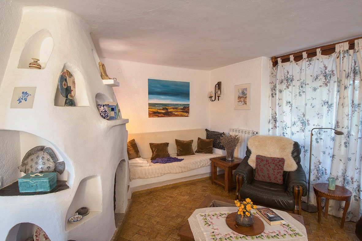 Rustic living area featuring a sculptural white-plastered fireplace with built-in niches, traditional clay tile flooring, and comfortable seating.