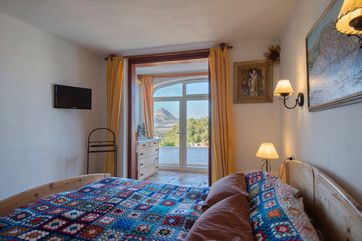Rustic-style bedroom featuring wooden furniture, a handcrafted bedspread, and direct access to a terrace with clear mountain views.
