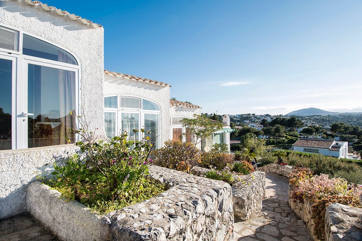 Traditional exterior featuring natural stone retaining walls, arched windows, and a paved pathway offering panoramic views of the surrounding valley.