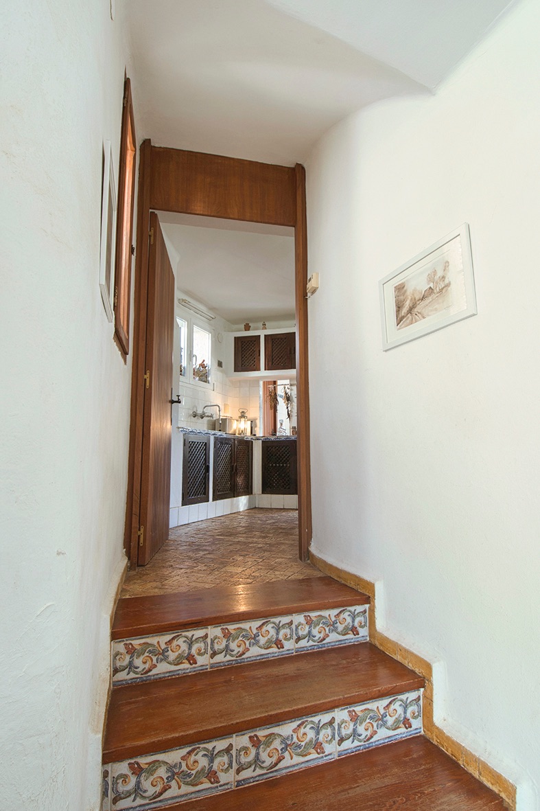 Wooden staircase with decorative tiled risers leading to a rustic kitchen featuring dark wood lattice cabinets and traditional flooring.