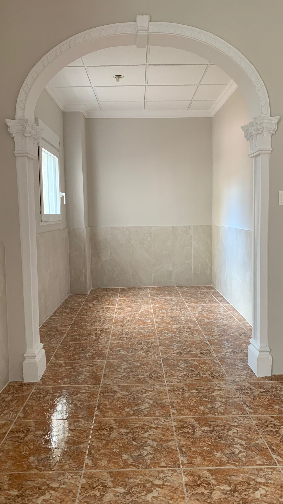 Entryway featuring a decorative classical arch, terracotta-style ceramic flooring, and walls with light-toned tiled wainscoting.