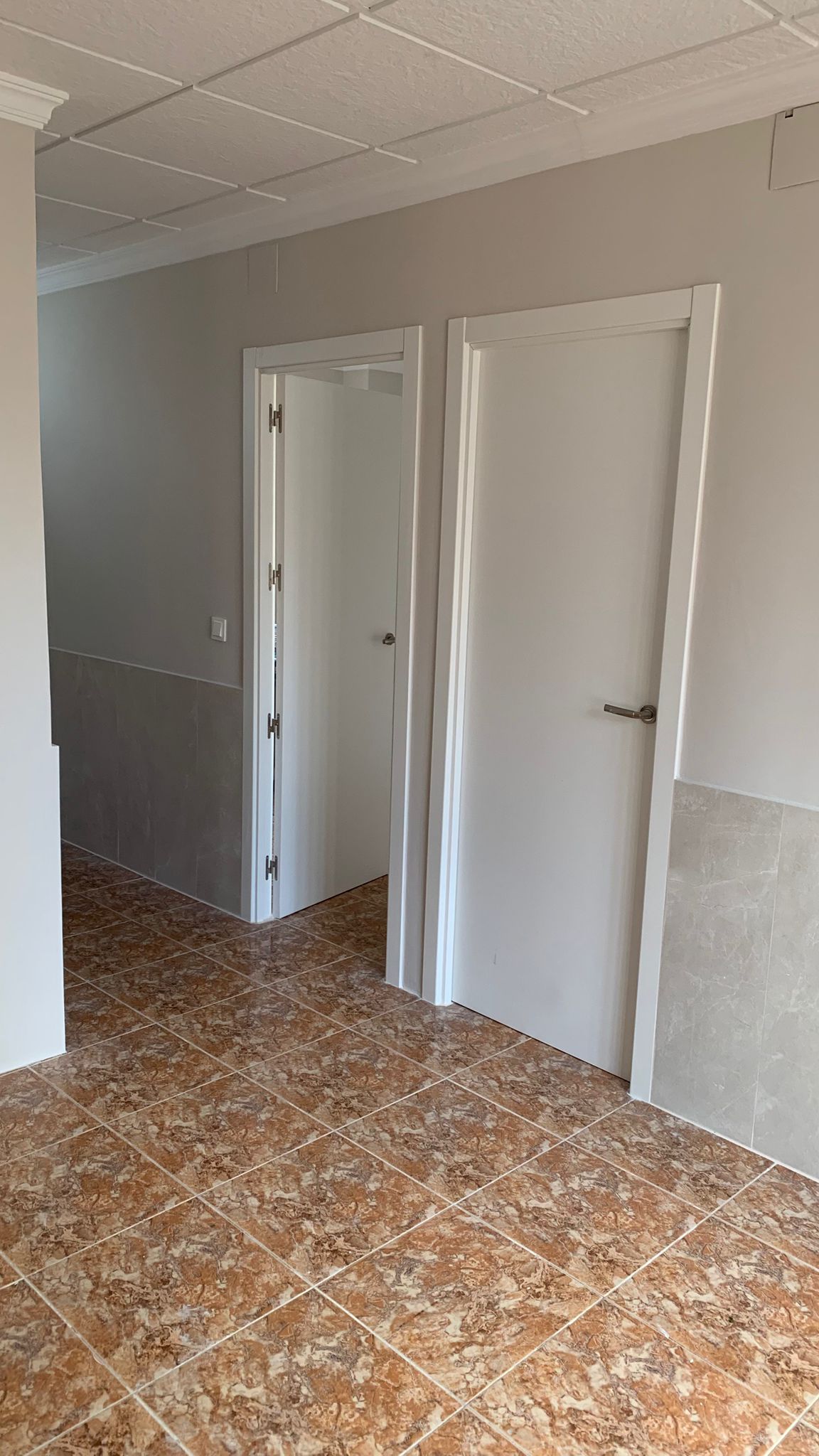 Hallway featuring marbled ceramic floor tiles, white interior doors with modern handles, and neutral-toned wall tiling for a clean finish.