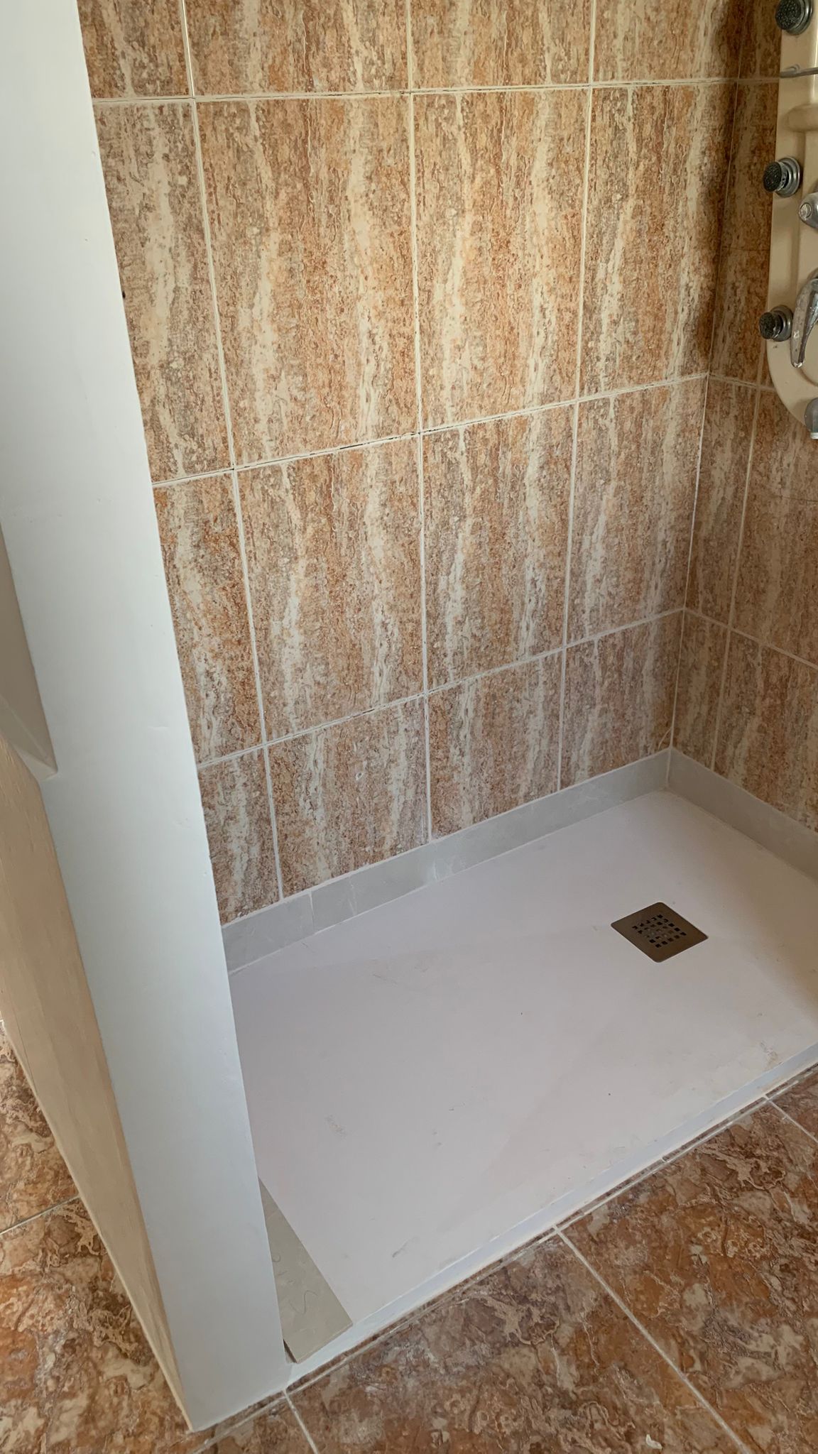 Modern walk-in shower featuring a white resin tray, vertical marble-effect wall tiles, and a functional hydromassage shower column.