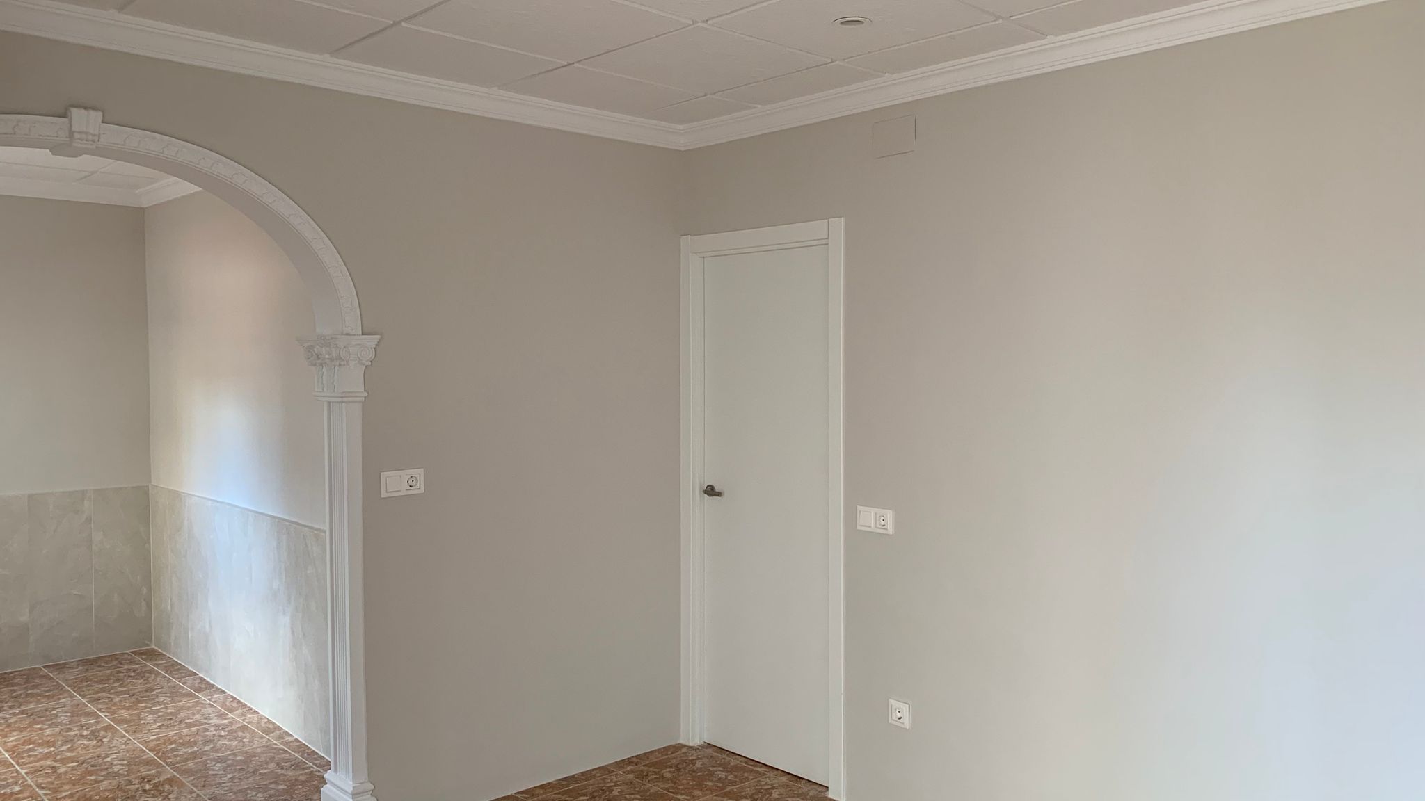 Renovated interior featuring neutral walls, tiled flooring, and a decorative white archway with classical moldings connecting the living spaces.