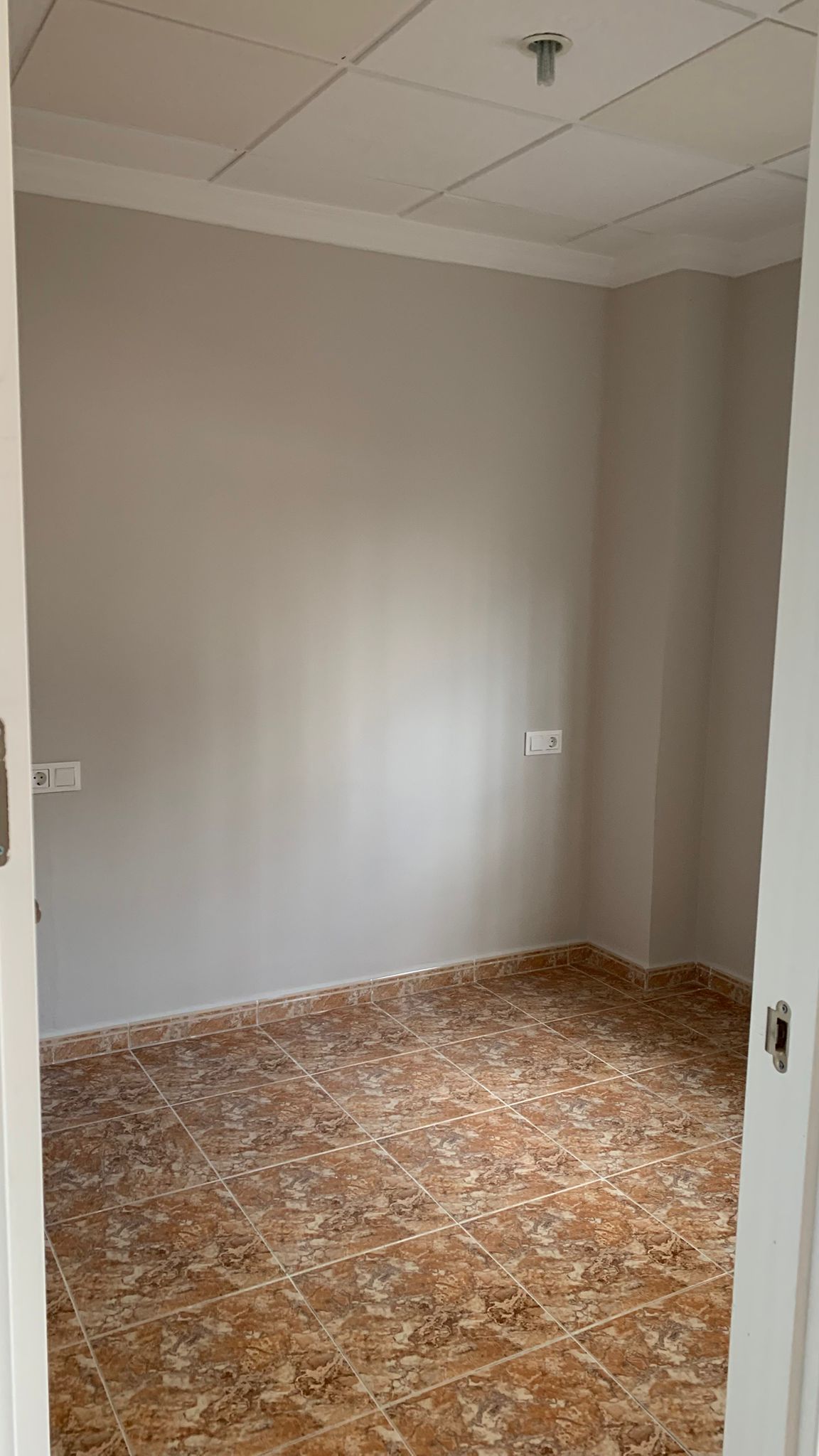 Renovated interior room featuring brown marble-effect ceramic floor tiles, neutral-toned walls, and a white grid drop ceiling.