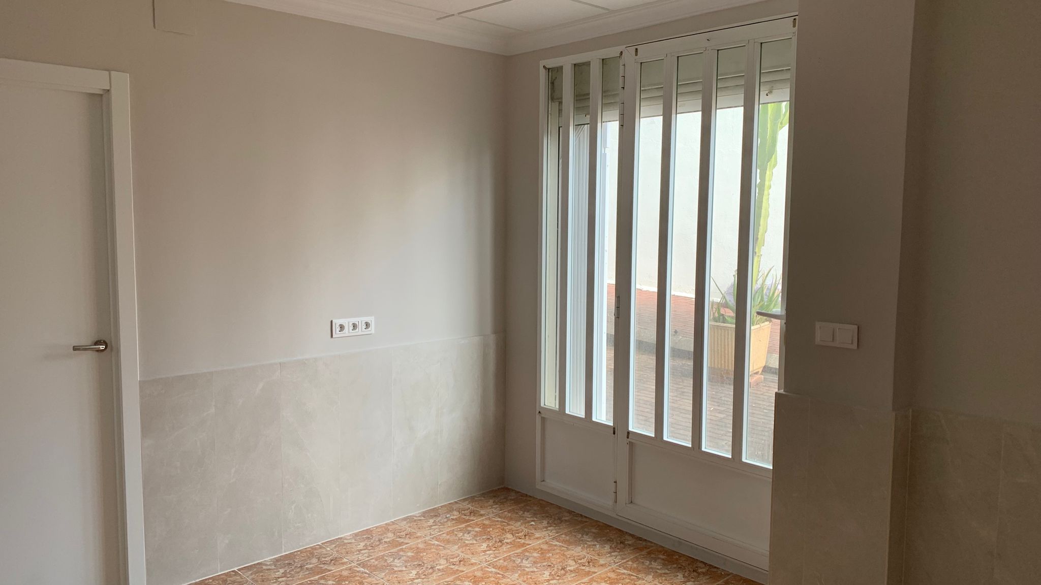 Room featuring tiled floors, half-height wall tiling, and a glass door with white security bars providing natural light and exterior access.