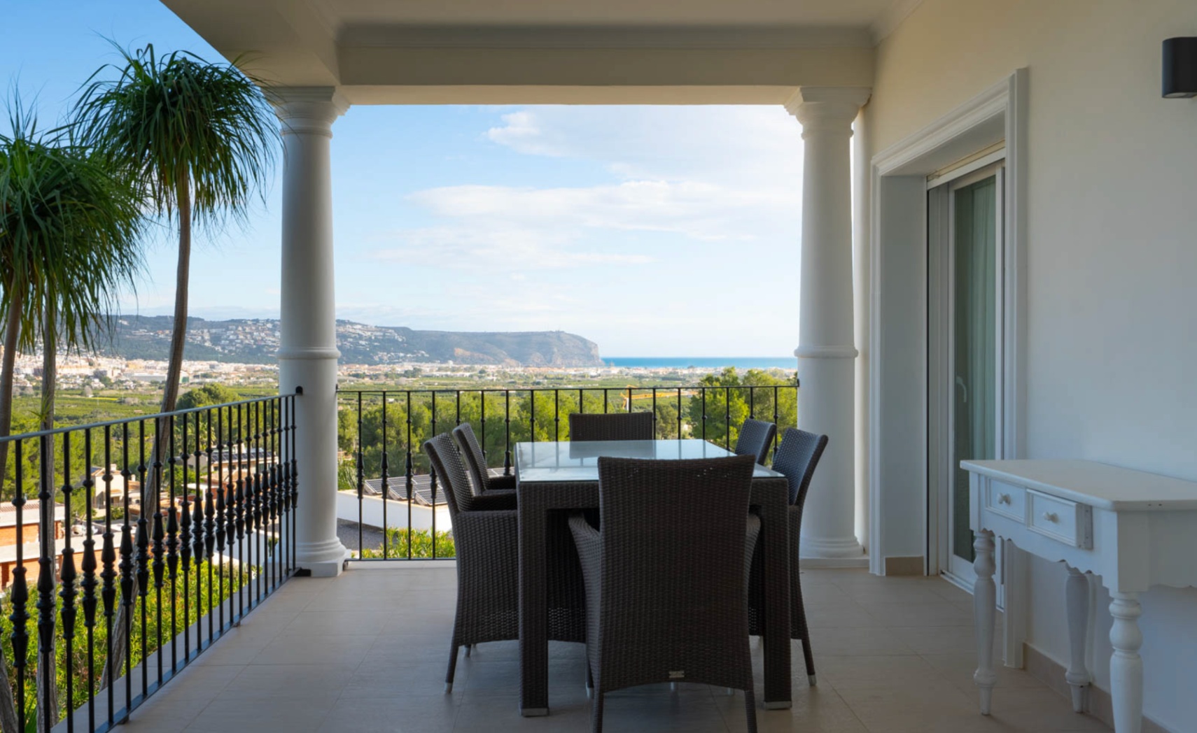 Covered terrace featuring classical white columns, wrought-iron railings, and a dining area with panoramic views of the Mediterranean Sea and Javea valley.