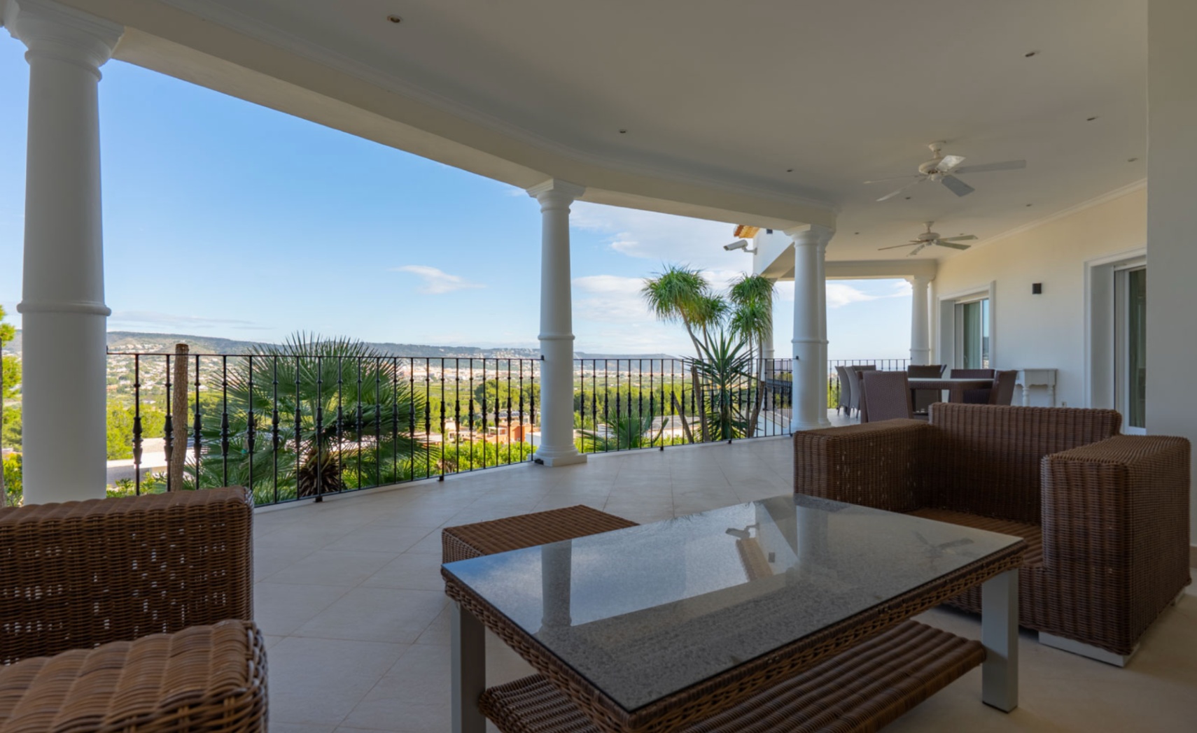 Covered terrace featuring white columns, wicker lounge furniture, and panoramic valley views. The space includes ceiling fans and recessed lighting for comfort.