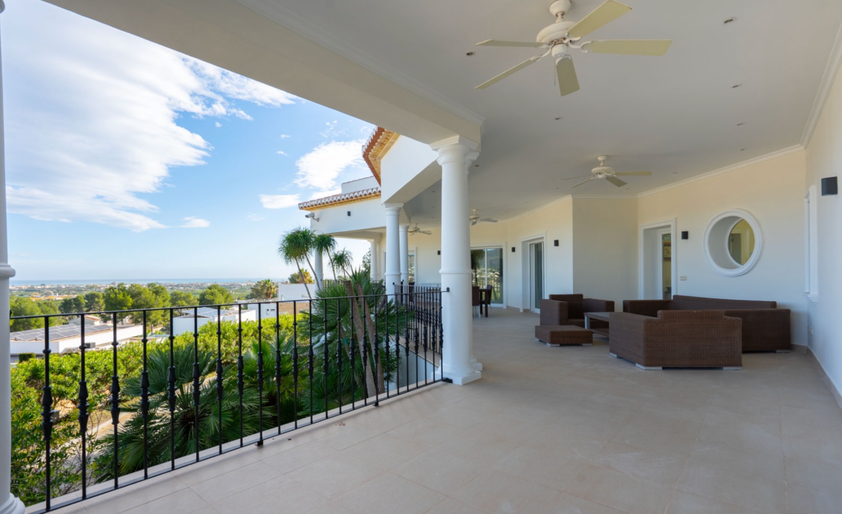 Covered terrace with white columns, ceiling fans, and outdoor lounge furniture, offering unobstructed views of the Mediterranean Sea and the coastline.