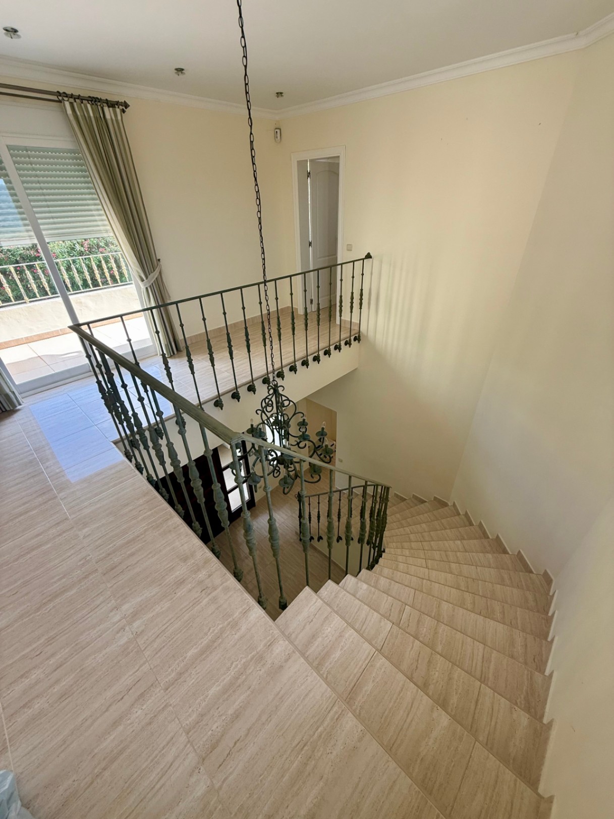 Curved marble staircase featuring a wrought iron railing and central chandelier, leading to a bright upper landing with terrace access.
