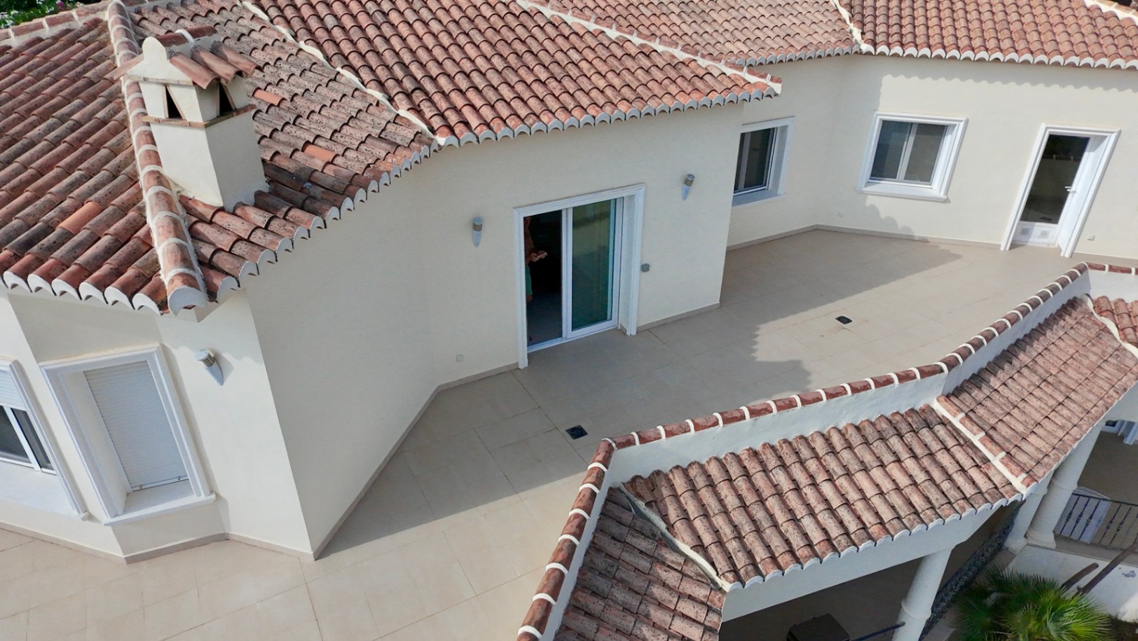 Elevated view of the upper terrace featuring ceramic tiling and sliding door access, showcasing the Mediterranean architecture with traditional terracotta roof tiles.