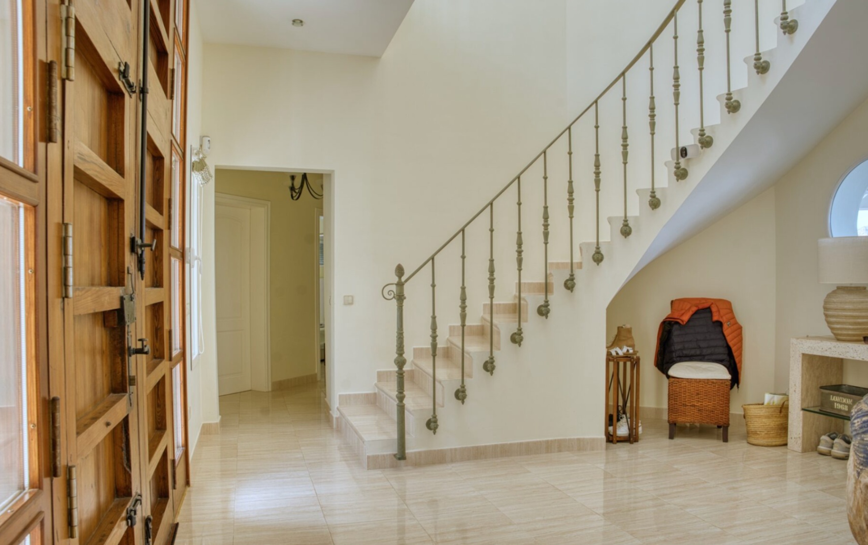 Entrance hall featuring a large solid wood door with glass inserts, polished stone flooring, and a curved staircase with a decorative wrought iron railing.