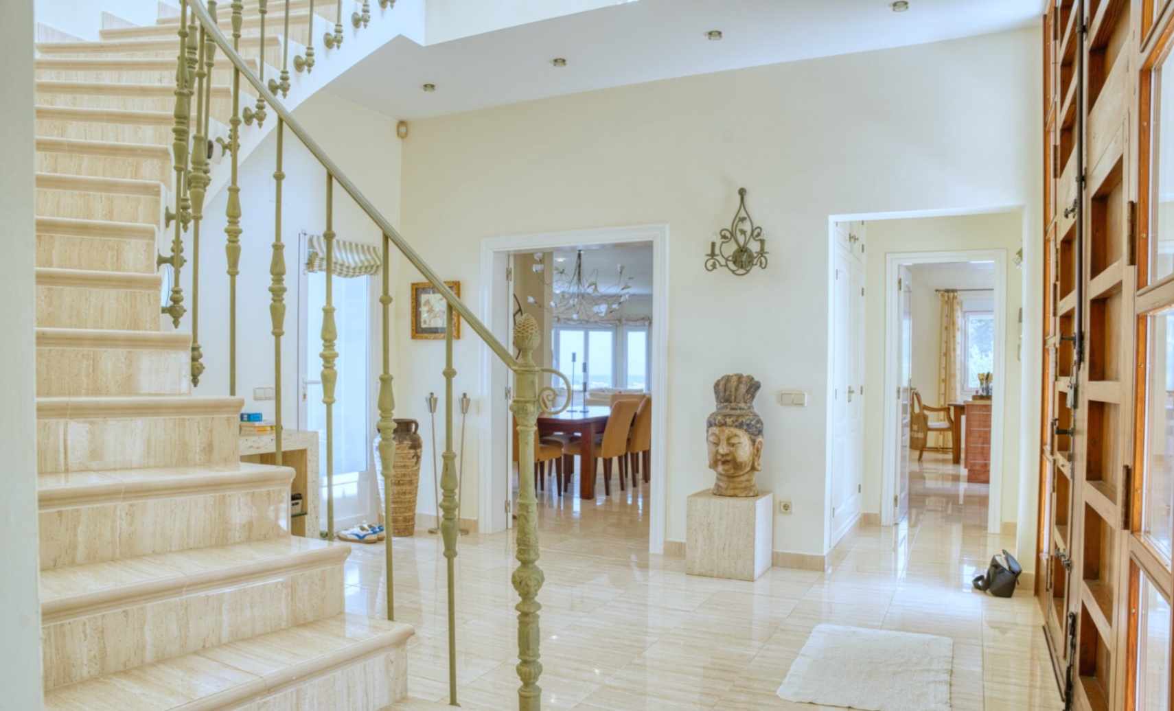 Entrance hall featuring a marble staircase with decorative wrought-iron railings. Polished stone floors lead to a dining area with sea views.