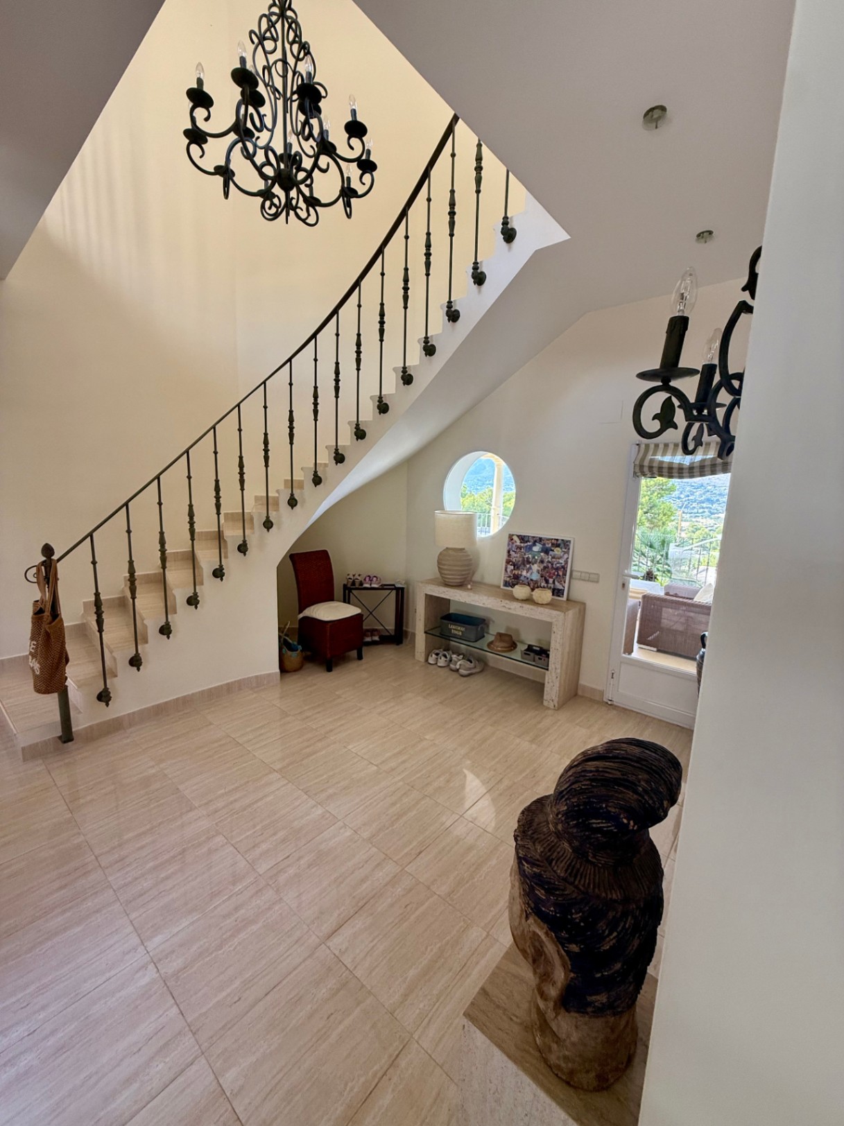 Entrance hall featuring marble flooring, a wrought iron staircase, and a circular window providing natural light and views towards the exterior terrace.